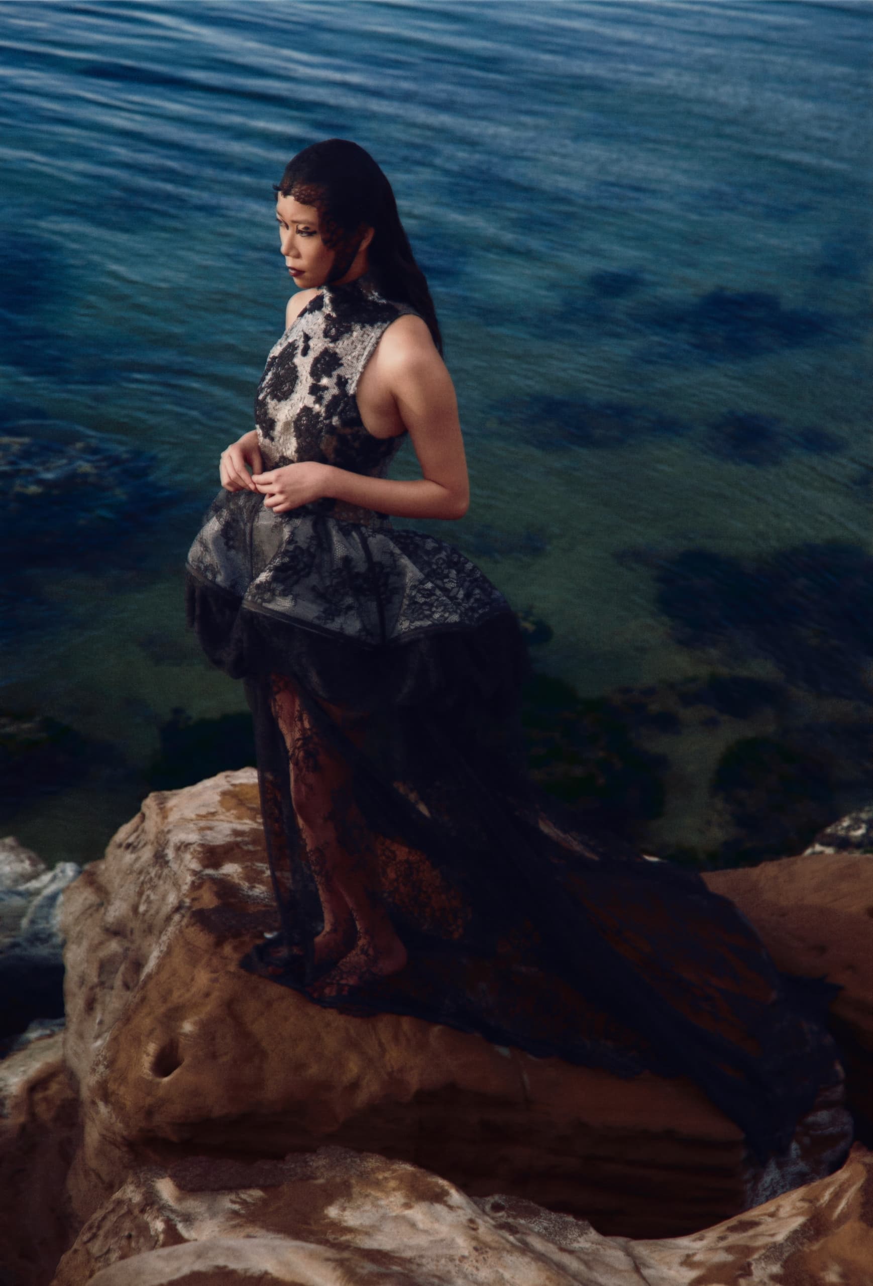 Woman in elegant dress standing on a rock by the sea.