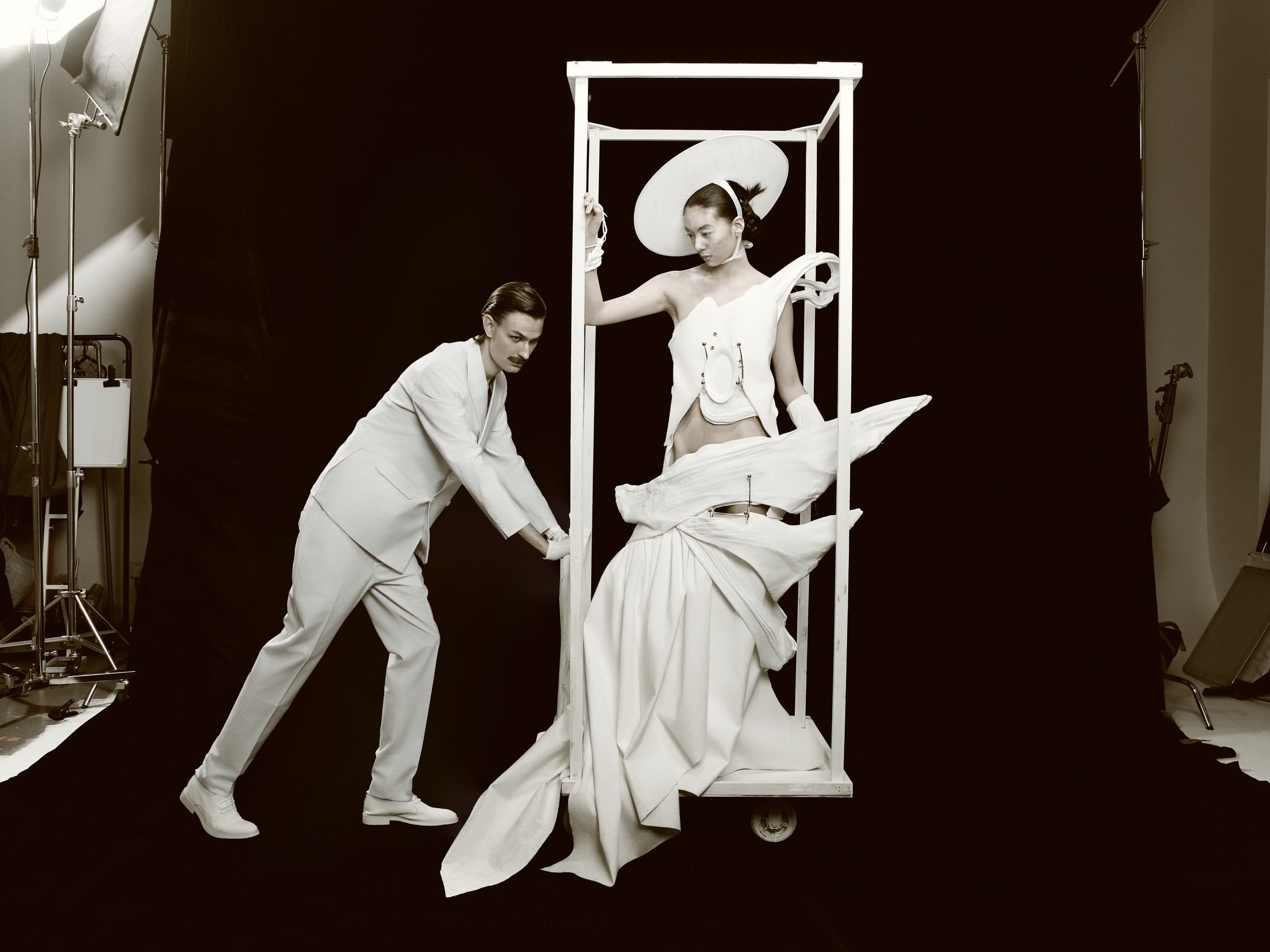 Man in suit pushing model in creative fashion outfit on set.