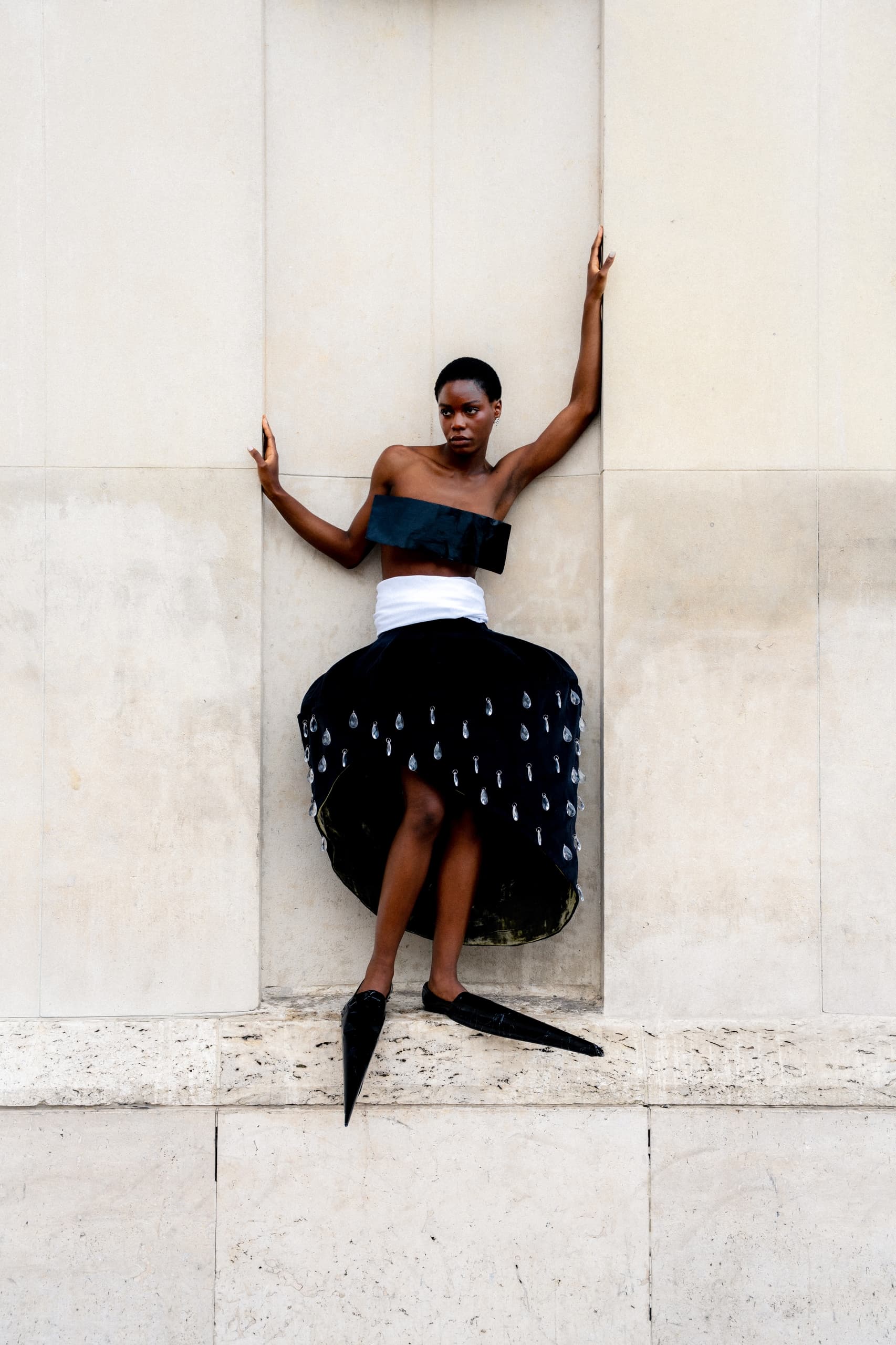 Model in avant-garde fashion outfit posing against a textured wall.