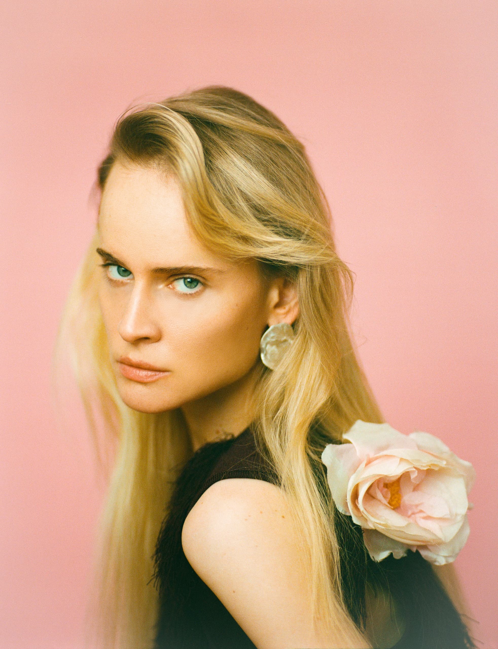 Woman with long hair and a flower in her hair, set against a pink background.