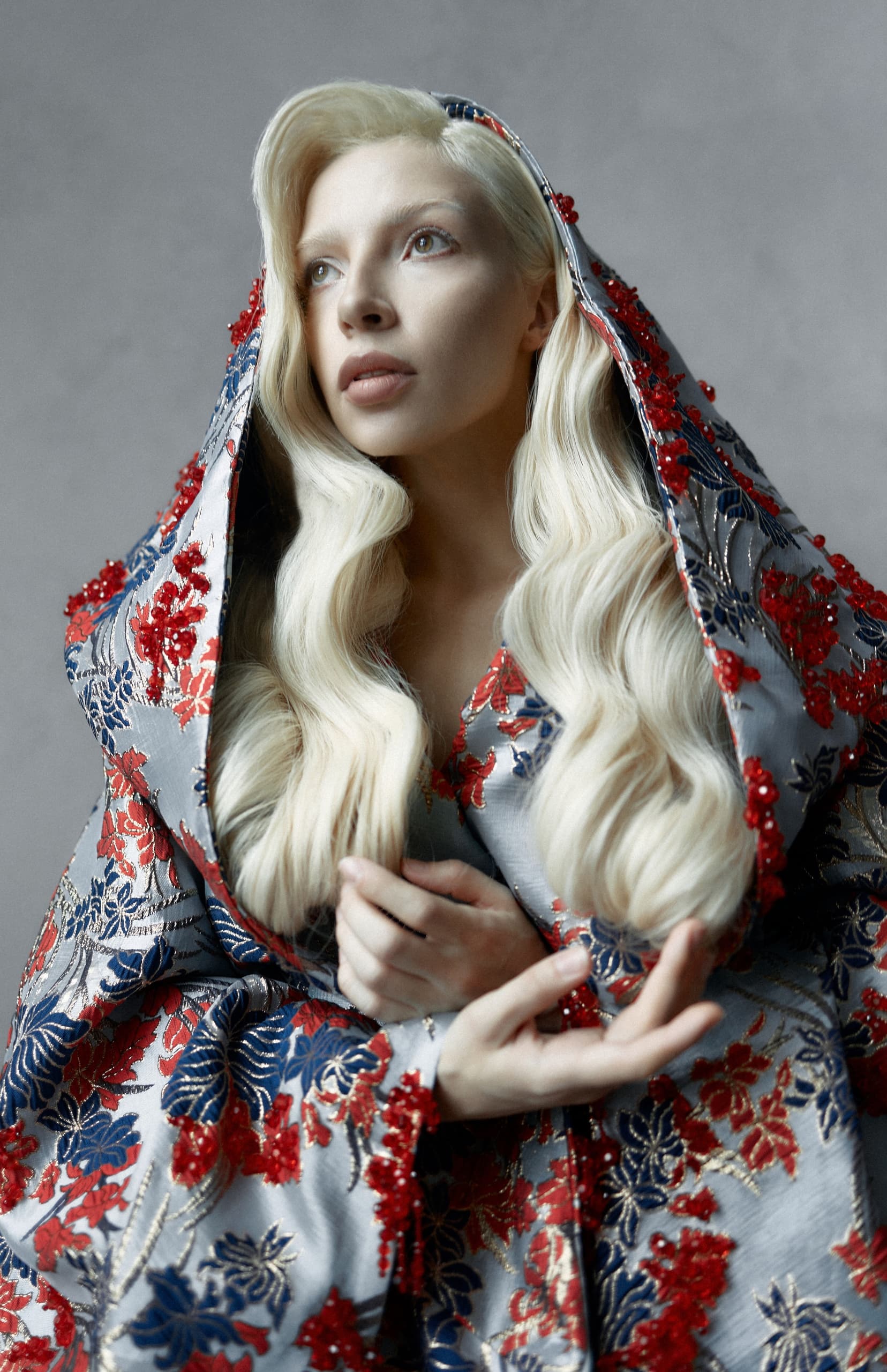 Elegant woman in floral embroidered cloak with blonde wavy hair.