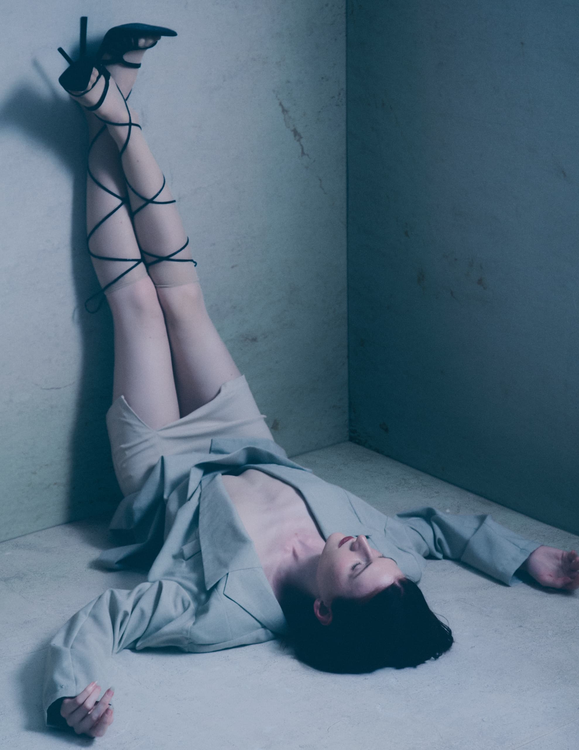 Woman in stylish suit and heels lying on floor with legs against wall.