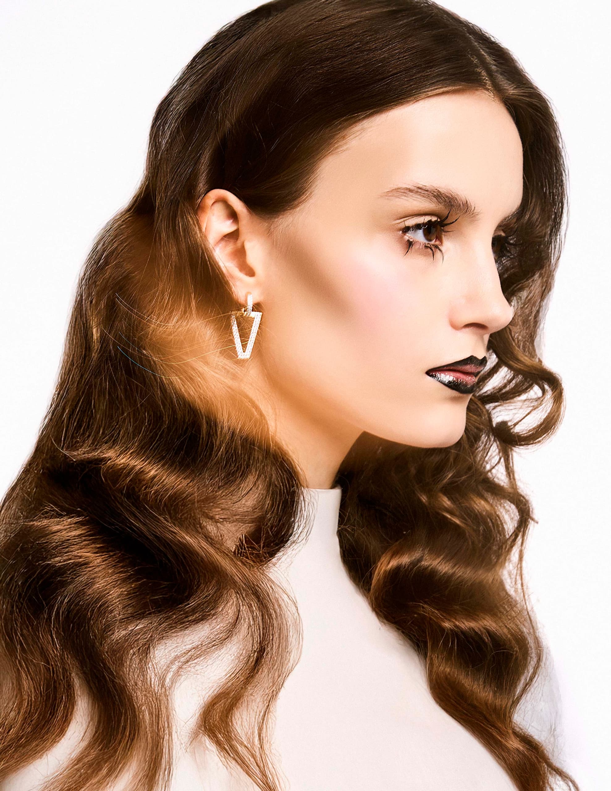 Profile of woman with long wavy hair, bold makeup, and geometric earring.