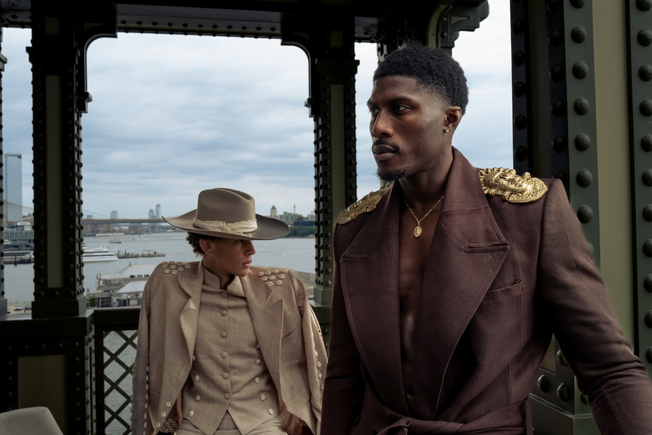 Stylish individuals in elegant attire on a bridge with a cityscape backdrop.