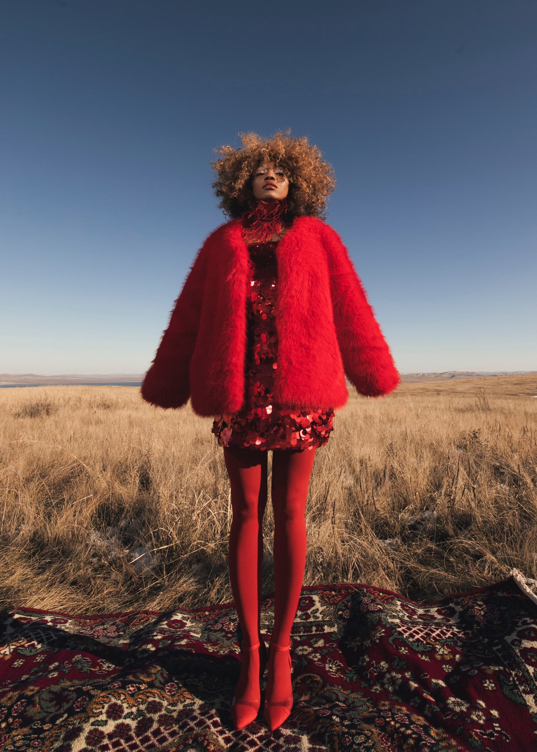 Woman in vibrant red outfit standing in an open field under a clear blue sky.