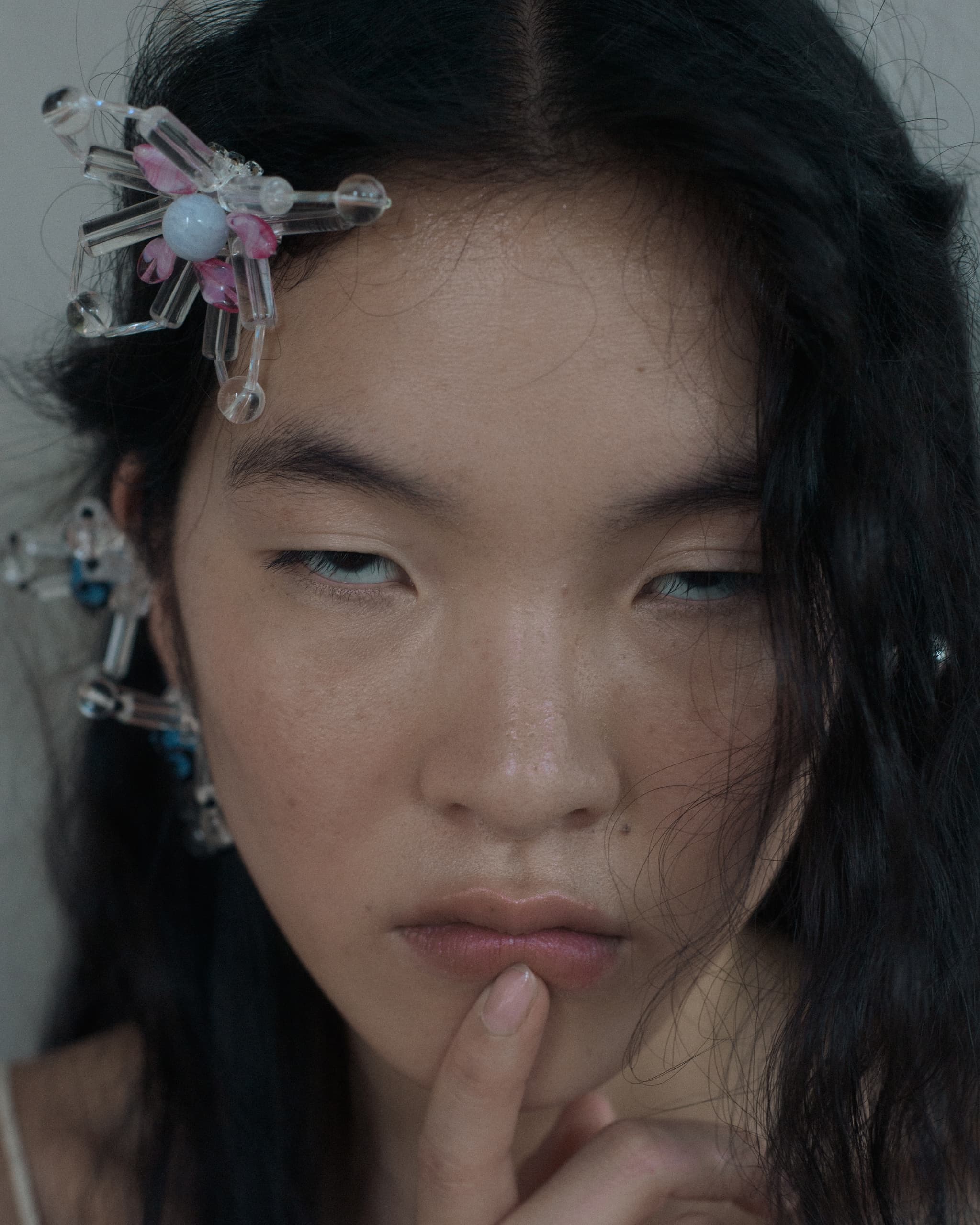 Woman with artistic hair clips and finger on lips, deep in thought.