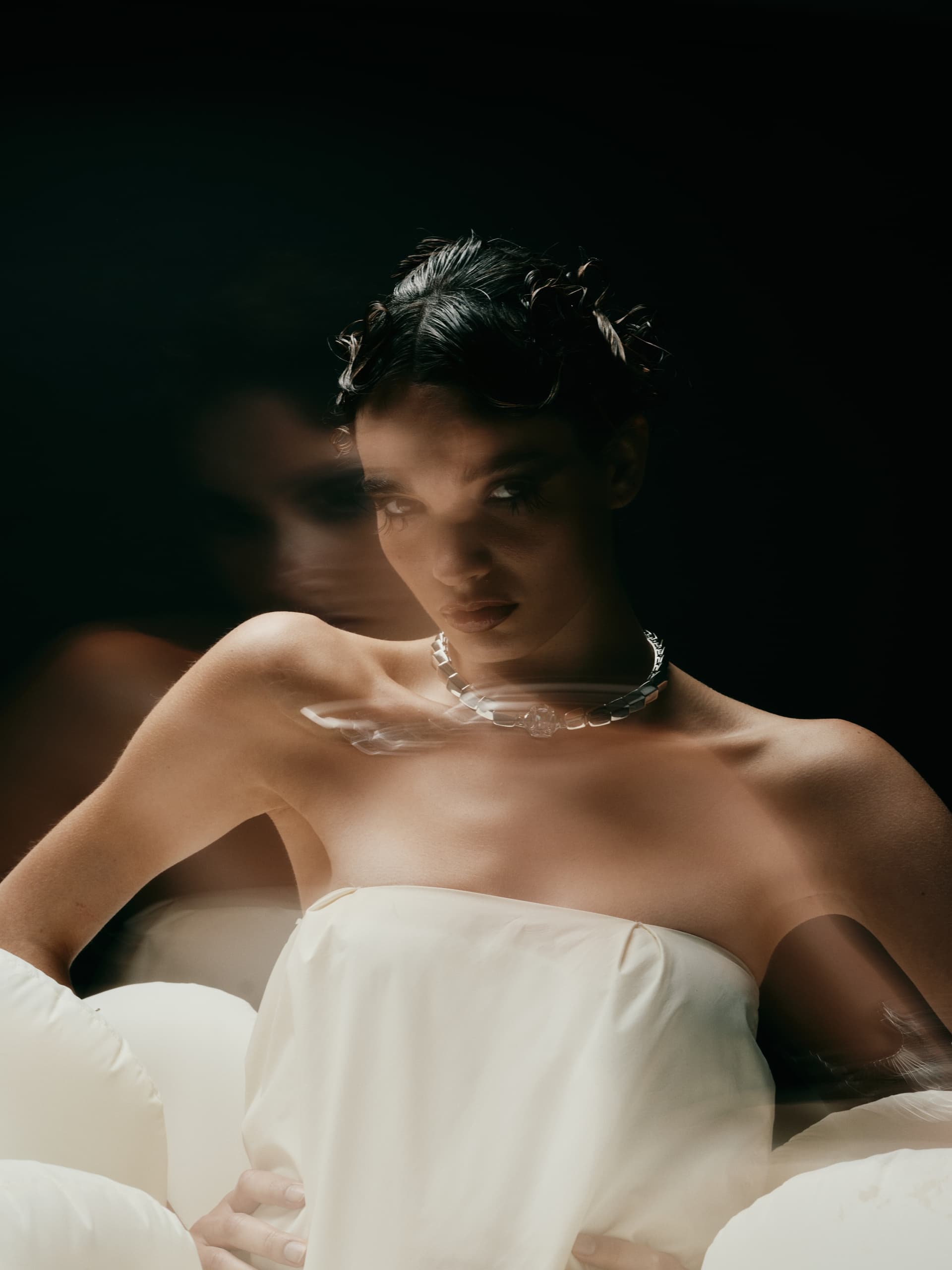 Artistic portrait of woman in motion, wearing a strapless dress against a dark background.