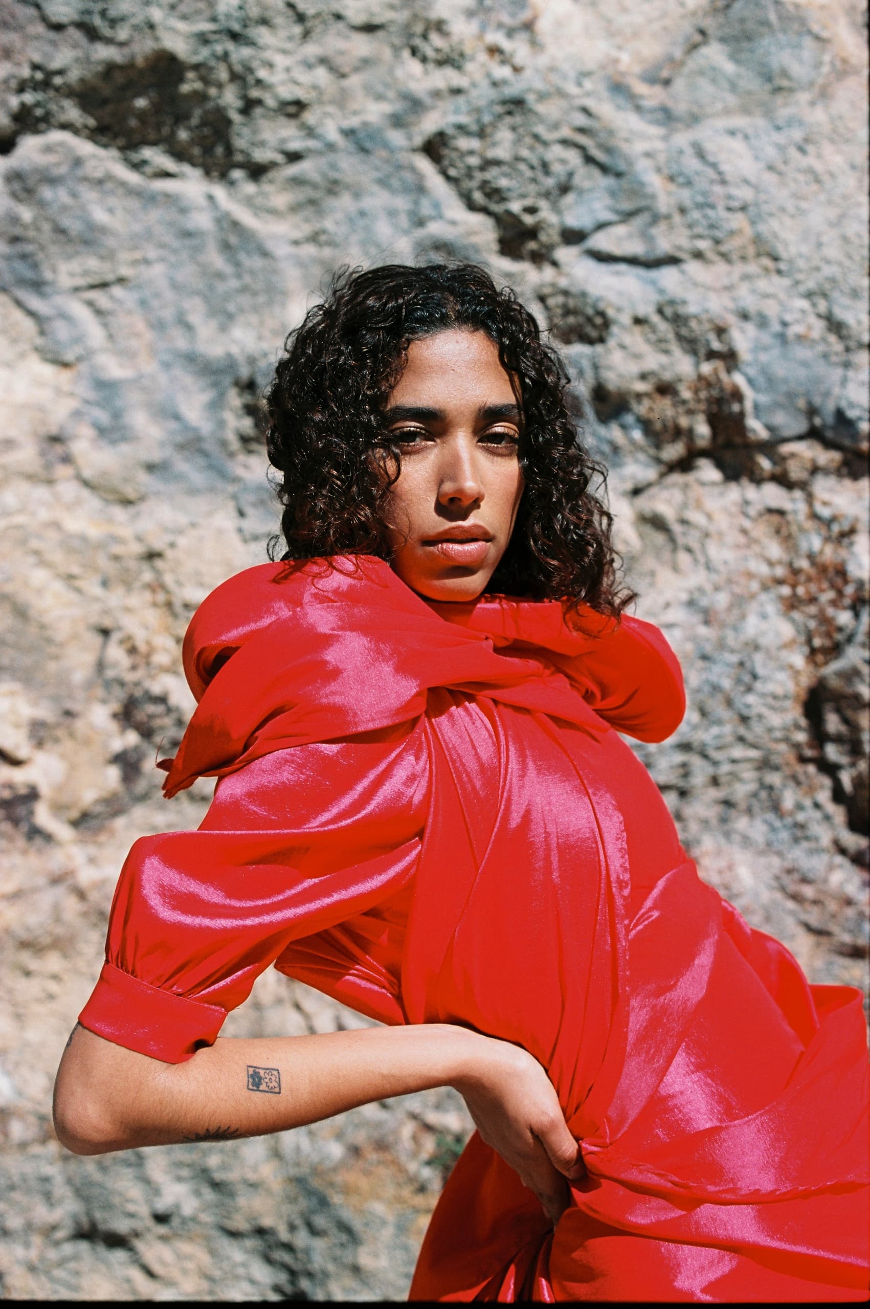 Woman in vibrant red dress poses against textured rocky background