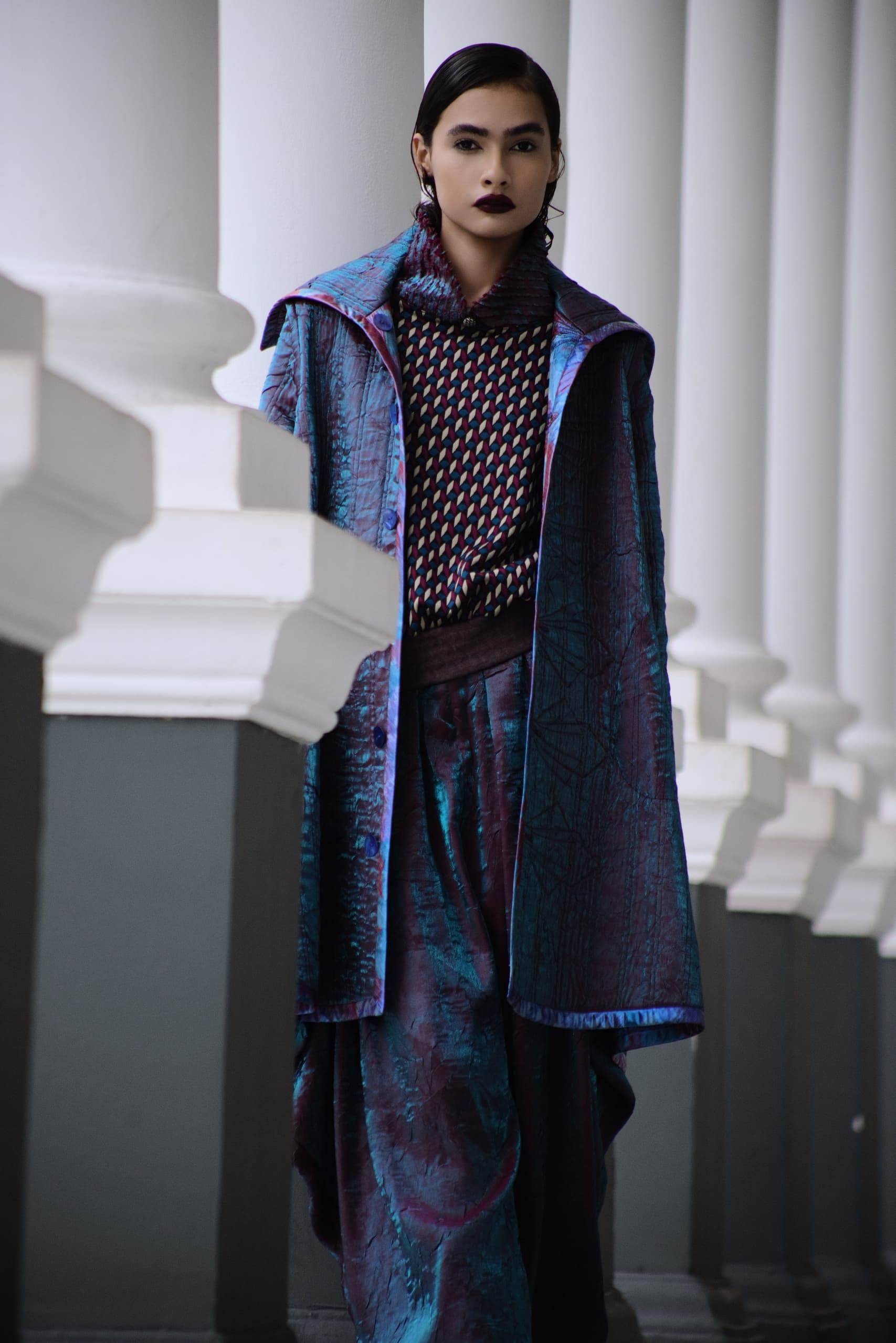 Fashionable woman in stylish blue and purple outfit next to white columns.
