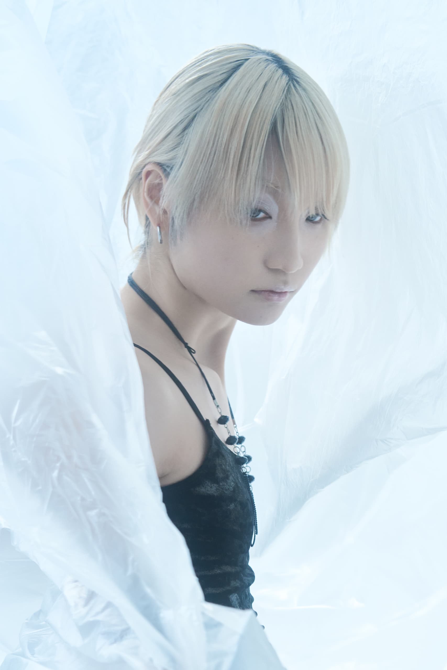 Person in stylish outfit stands among delicate white sheets, creating an ethereal look.