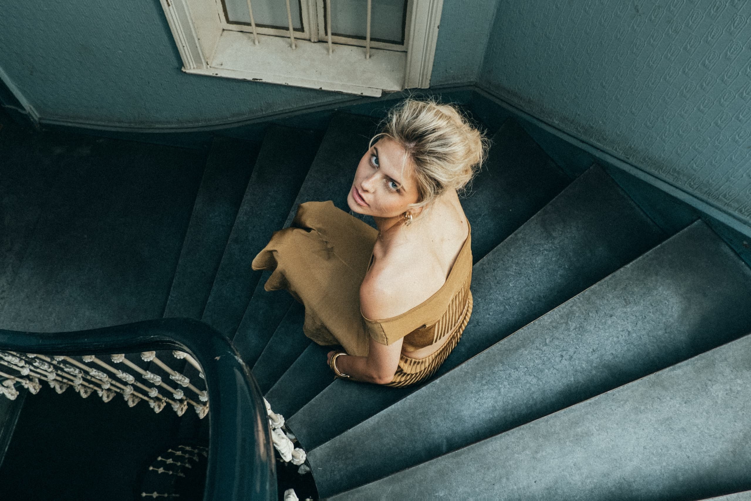Woman in a brown dress on spiral staircase, looking upward.