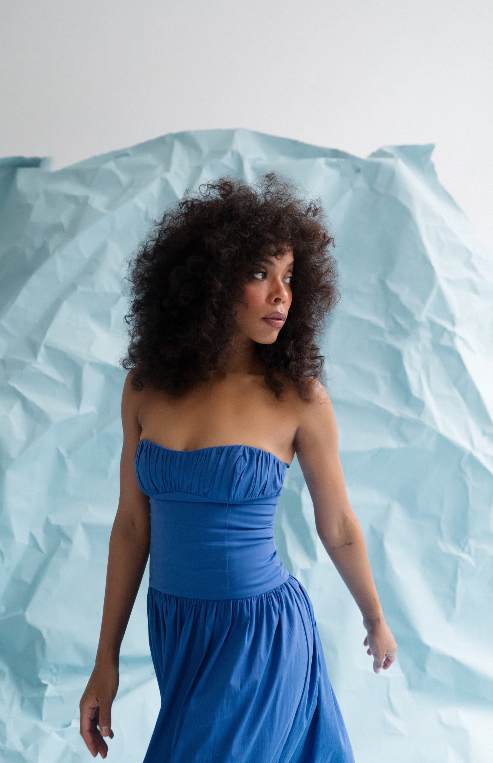 Woman in blue dress standing against a textured blue backdrop.
