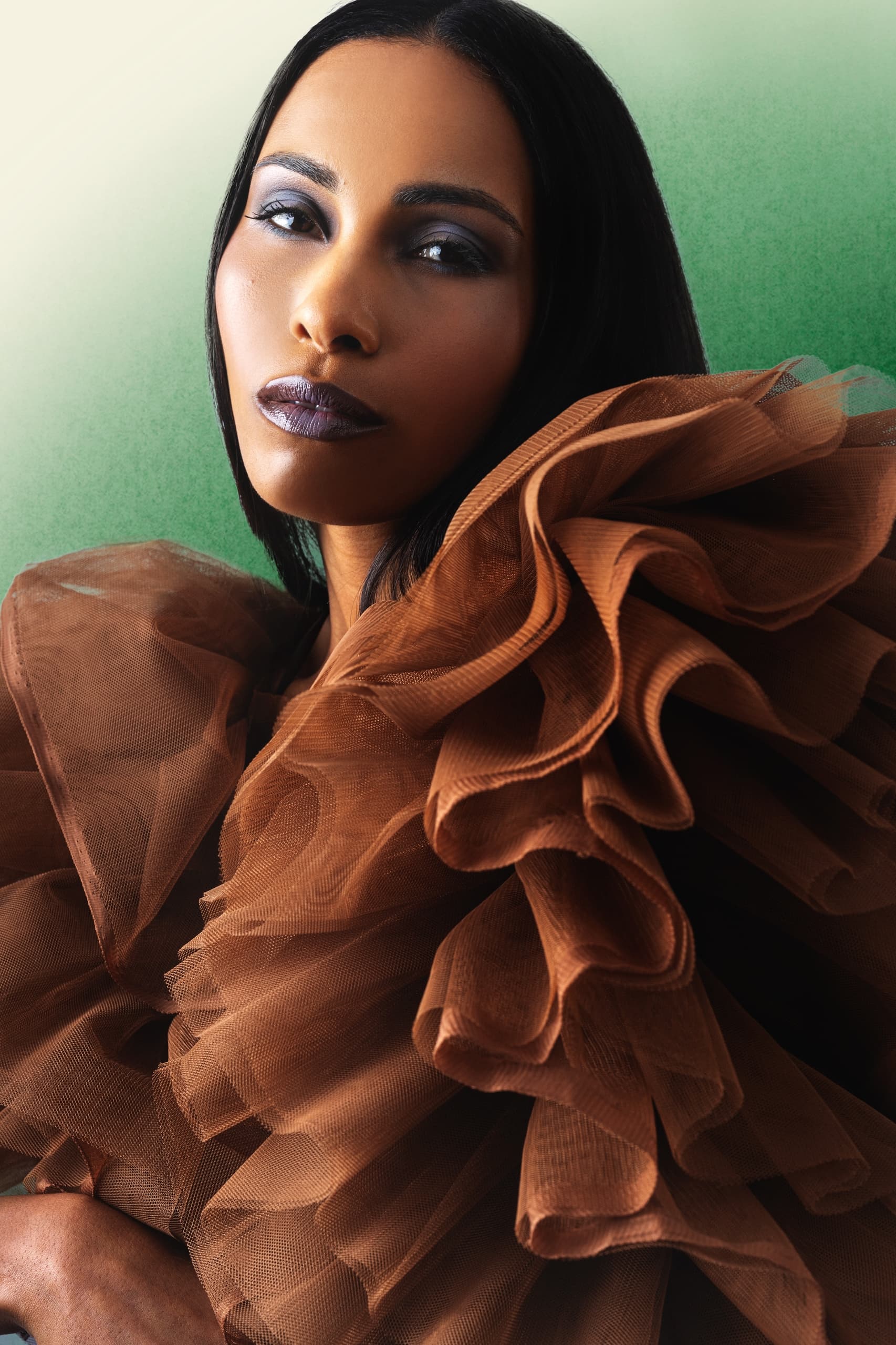 Elegant model in a brown ruffled dress with a green background. Fashion photography.