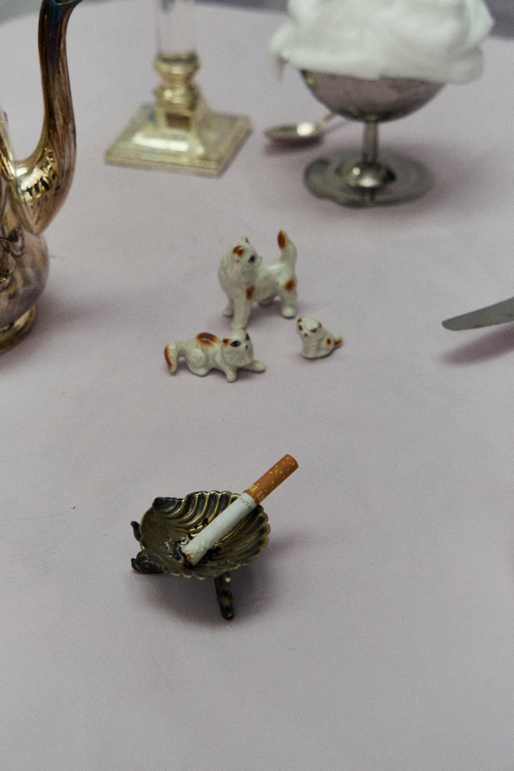 Cigarette in ashtray with porcelain cats and teapot on table.