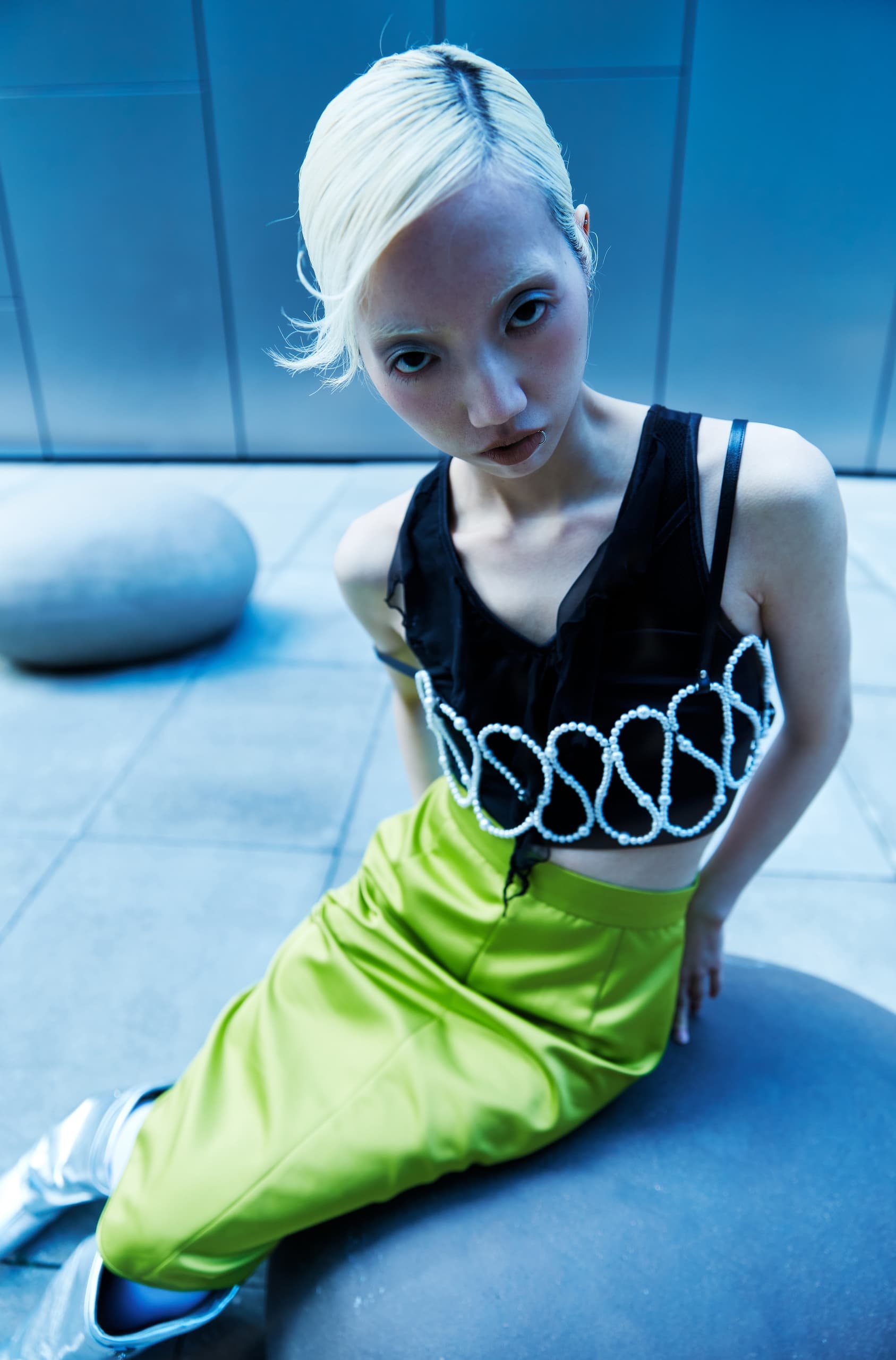 Fashionable person in pearl-accented top and green skirt, sitting in a modern setting.