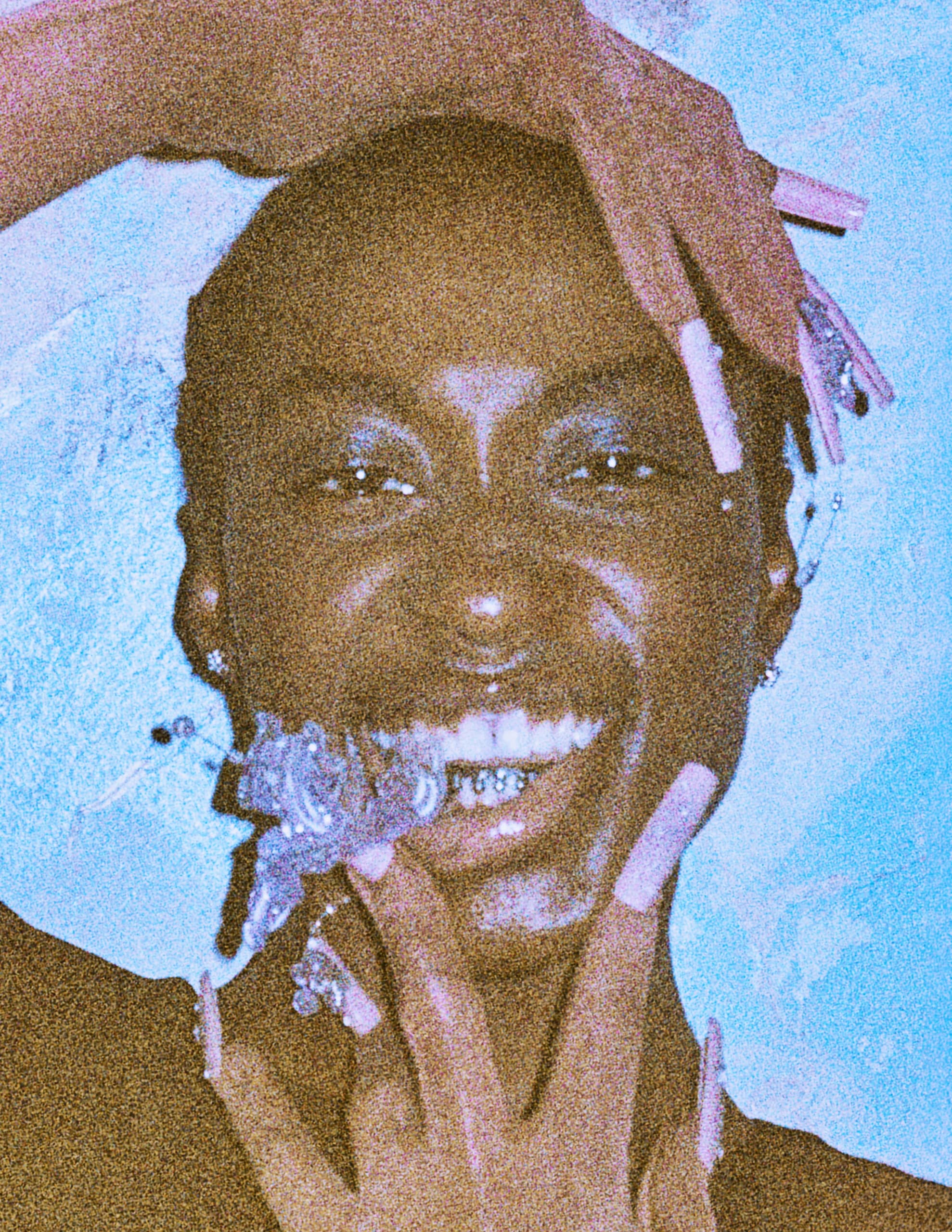 Smiling person with long nails and artistic makeup in a colorful, creative setting.