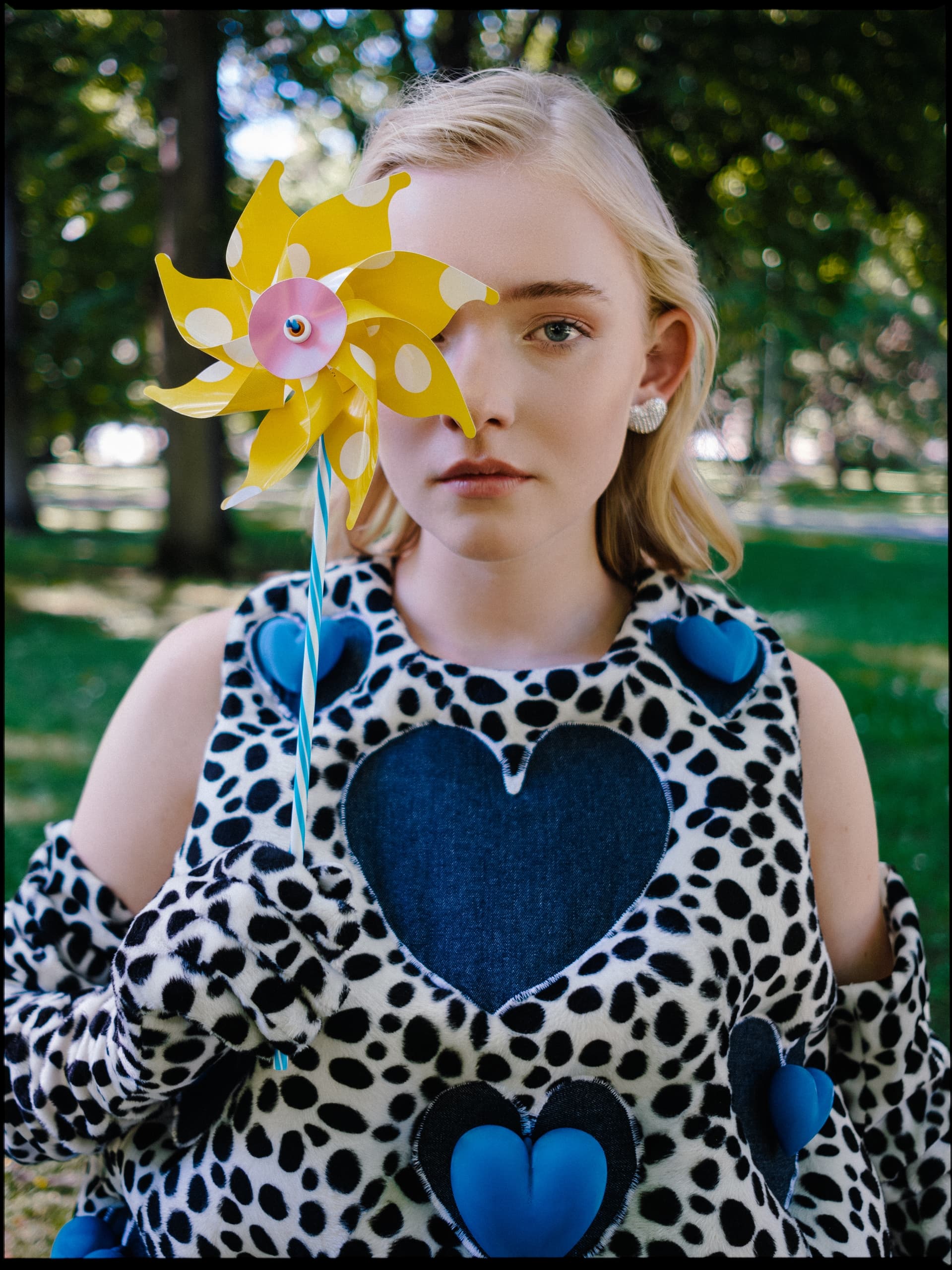 Fashionable woman with yellow pinwheel in park, wearing heart-patterned outfit.