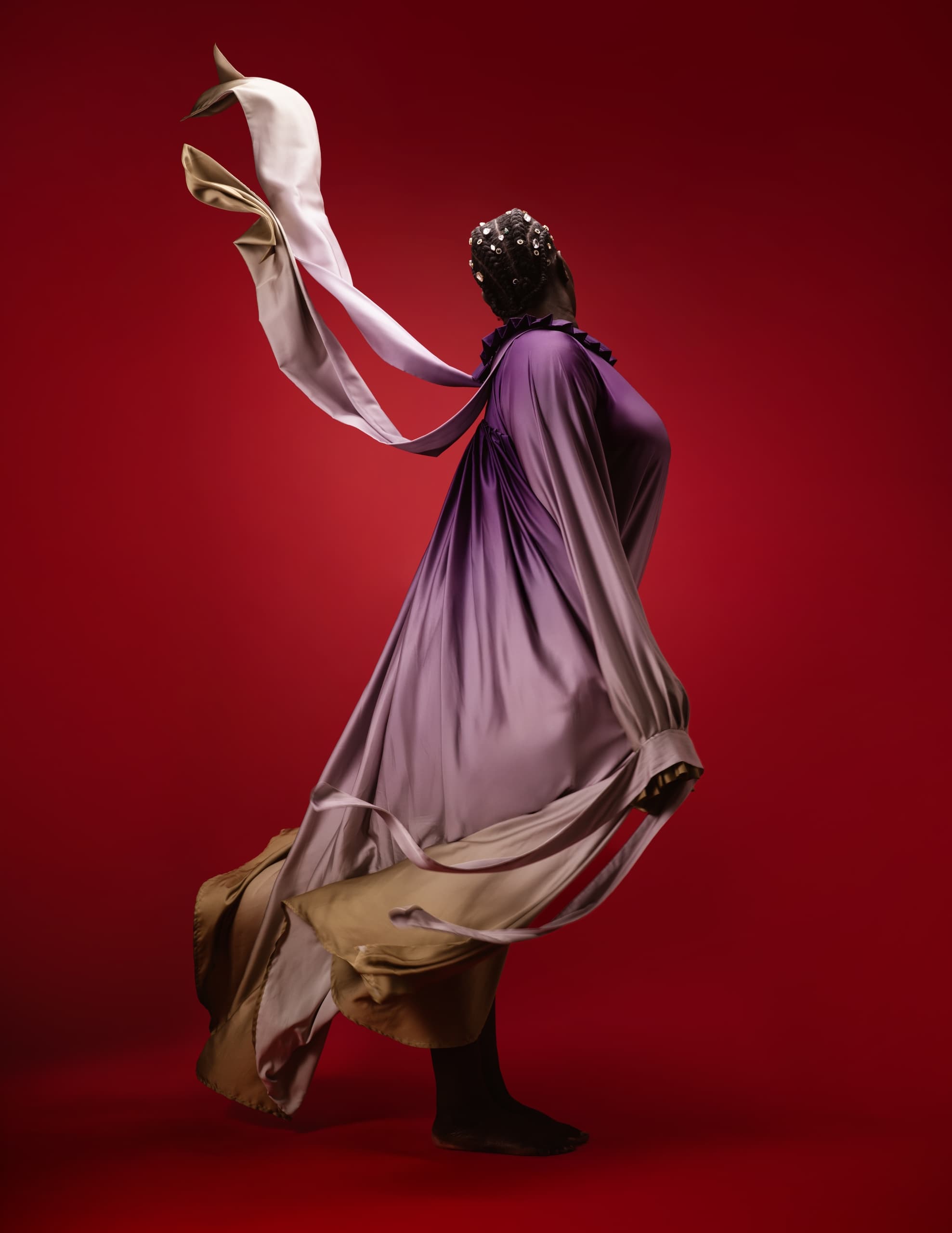 Elegant figure in flowing purple and beige dress on a vibrant red background.