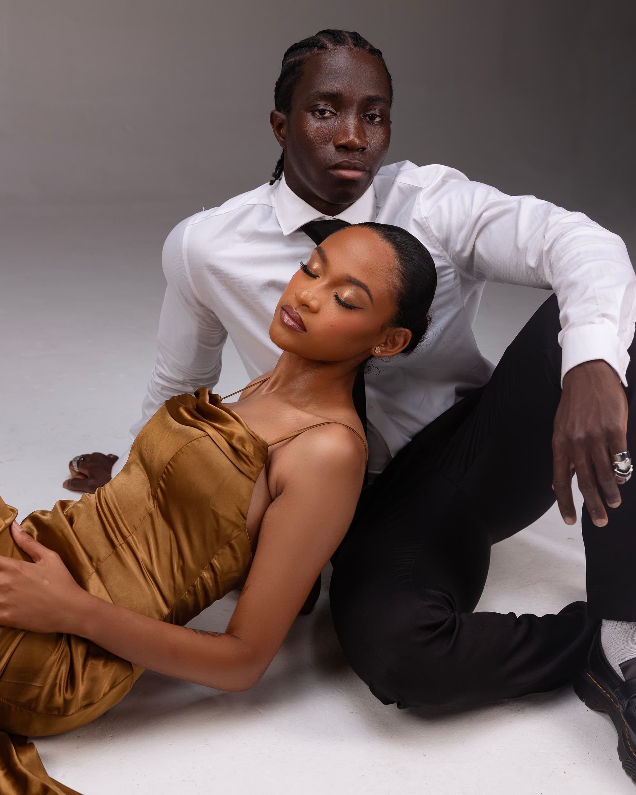 Elegant couple posing in stylish attire on a neutral background.