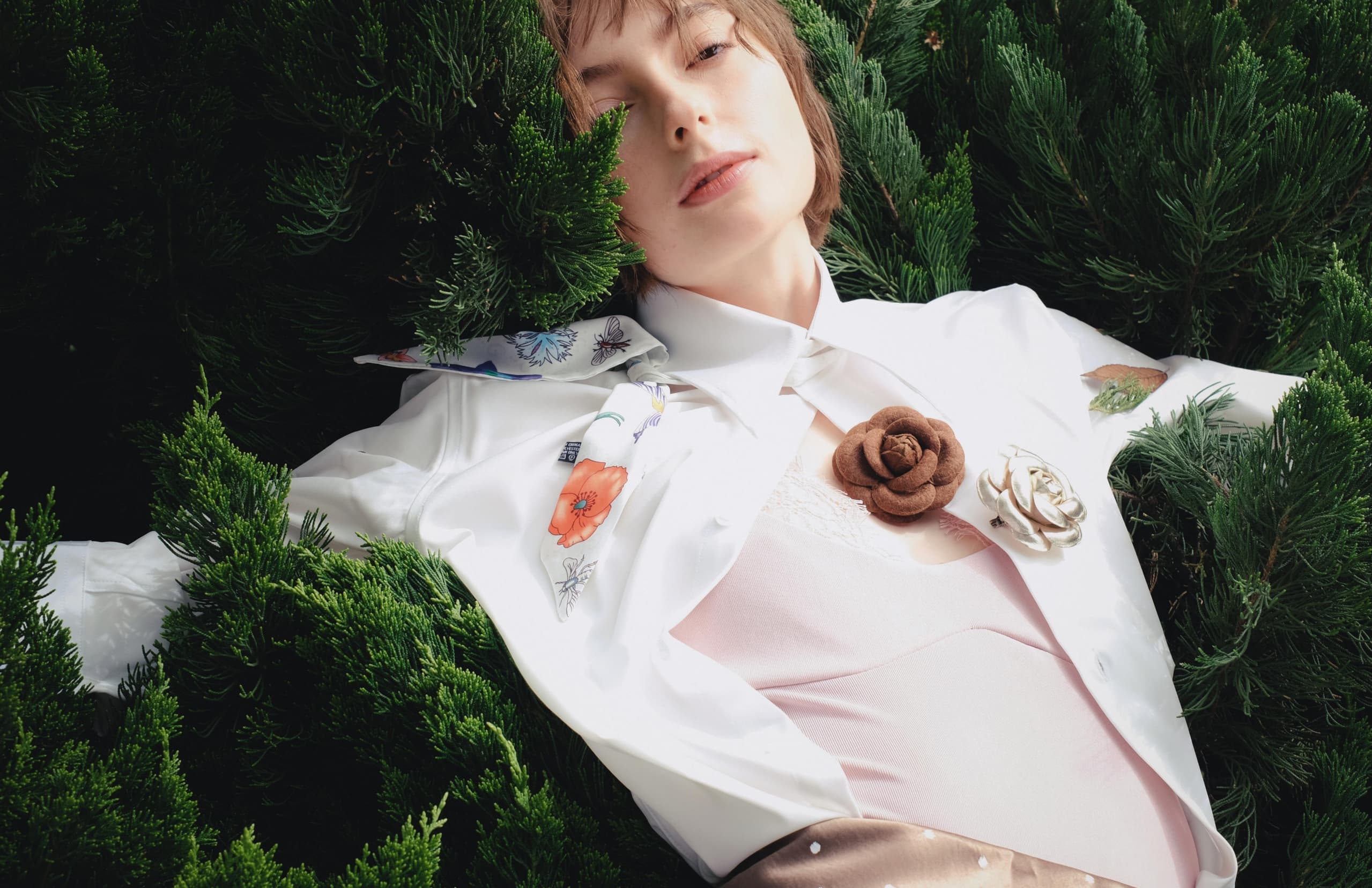 Fashionable woman in white blouse surrounded by evergreen leaves.