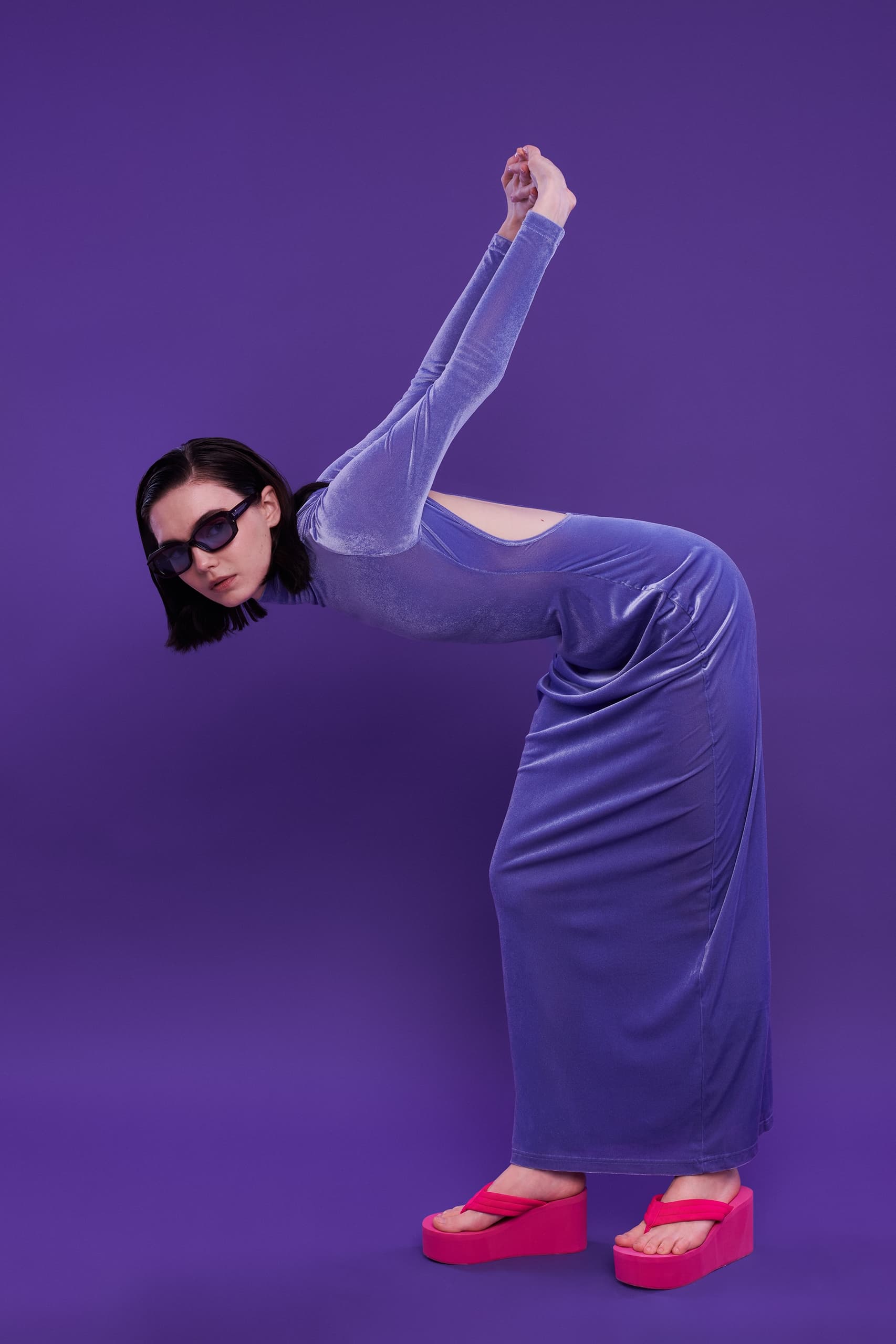 Person in a purple dress and sunglasses posing on purple background.
