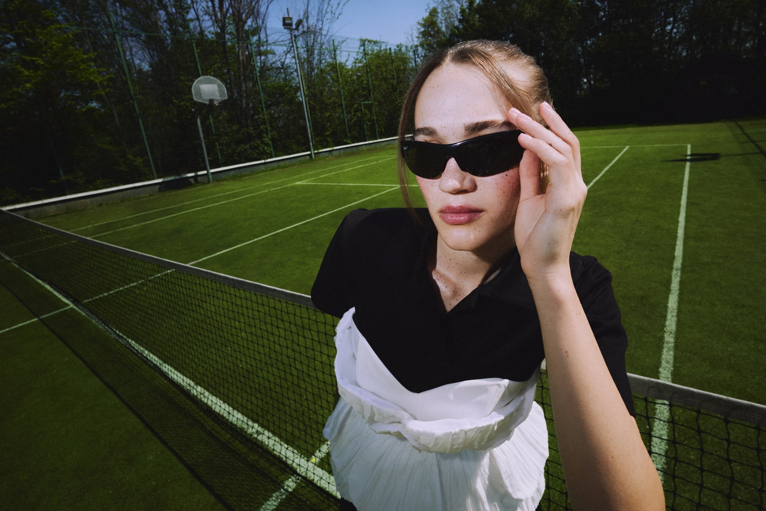 Woman in sunglasses on a grass tennis court by the net.