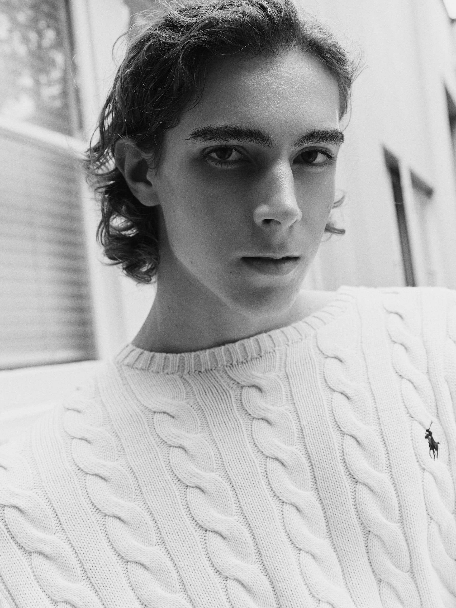 Portrait of a person in a white cable knit sweater, outdoor setting.
