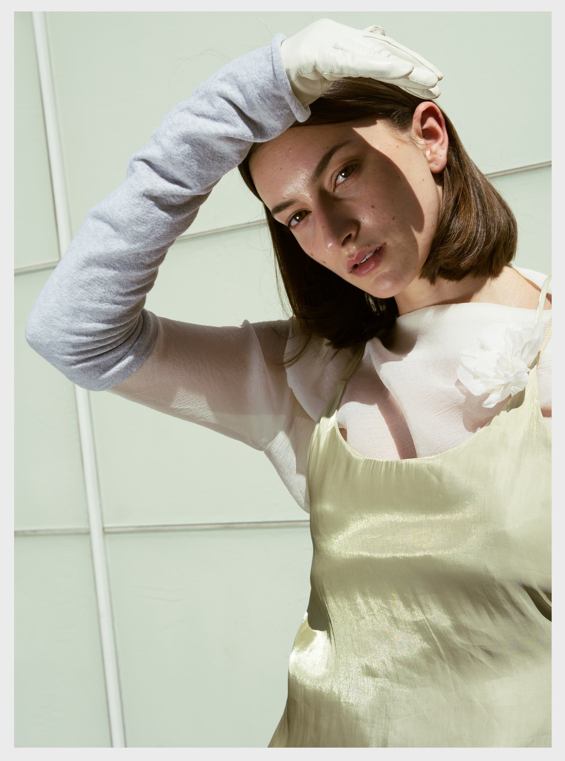 Woman poses in stylish light outfit, hand shielding eyes from sunlight.