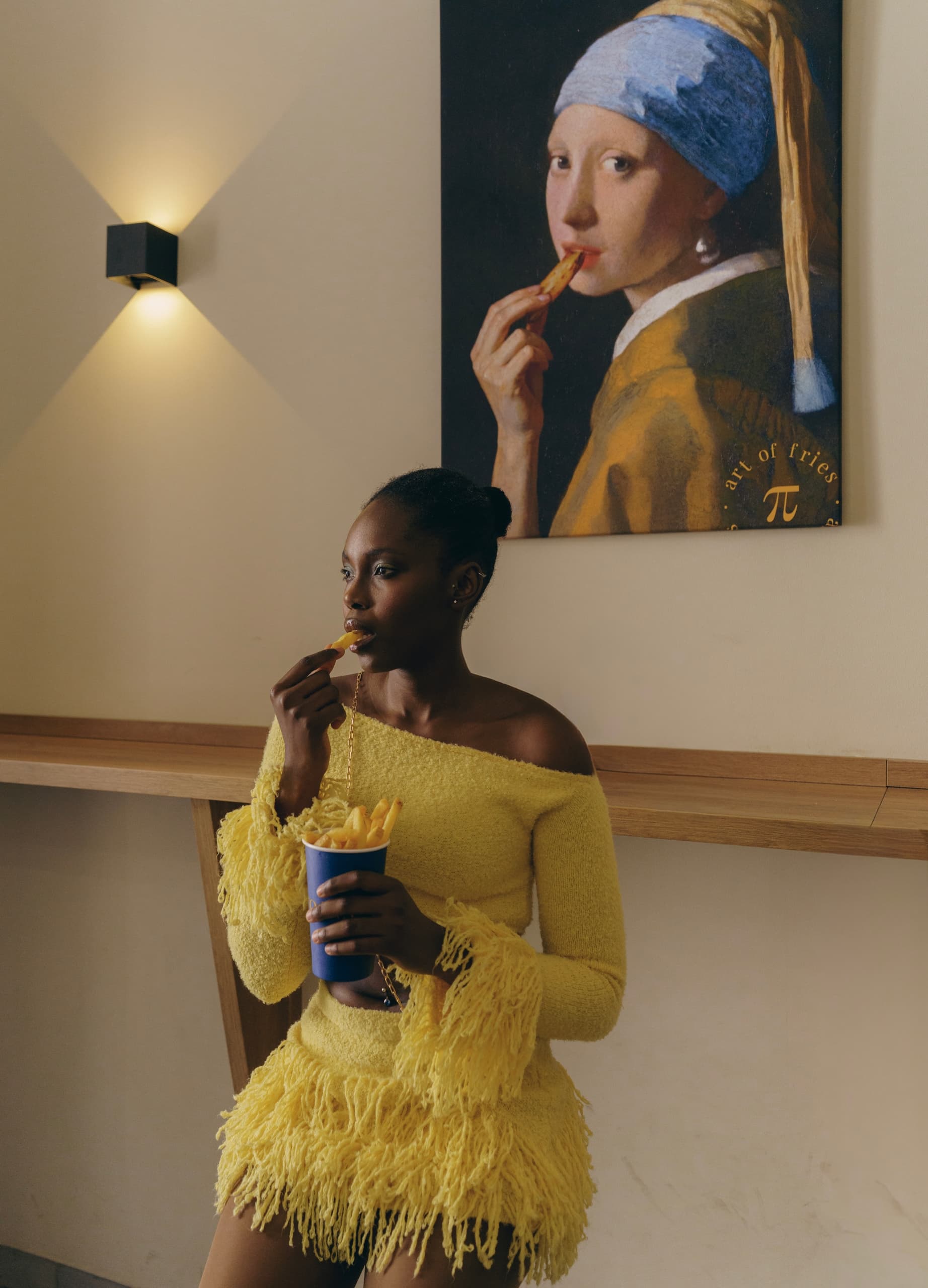 Woman eating fries, vibrant yellow outfit, art-inspired poster backdrop.