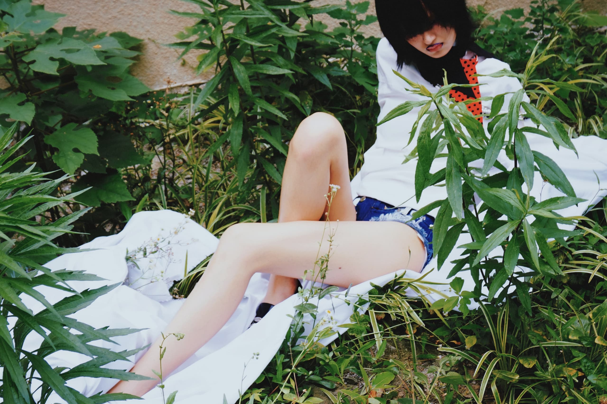 Person relaxing in greenery, wearing white shirt and denim shorts.