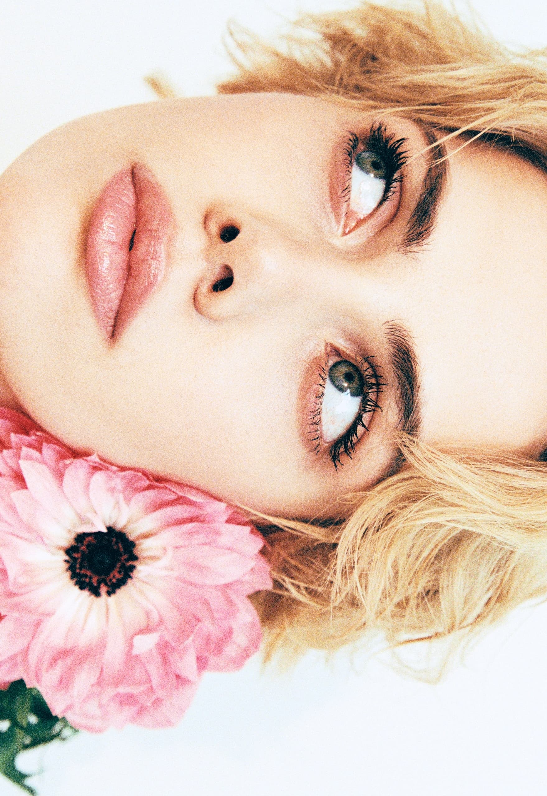 Woman with blonde hair and pink flower, looking upwards.