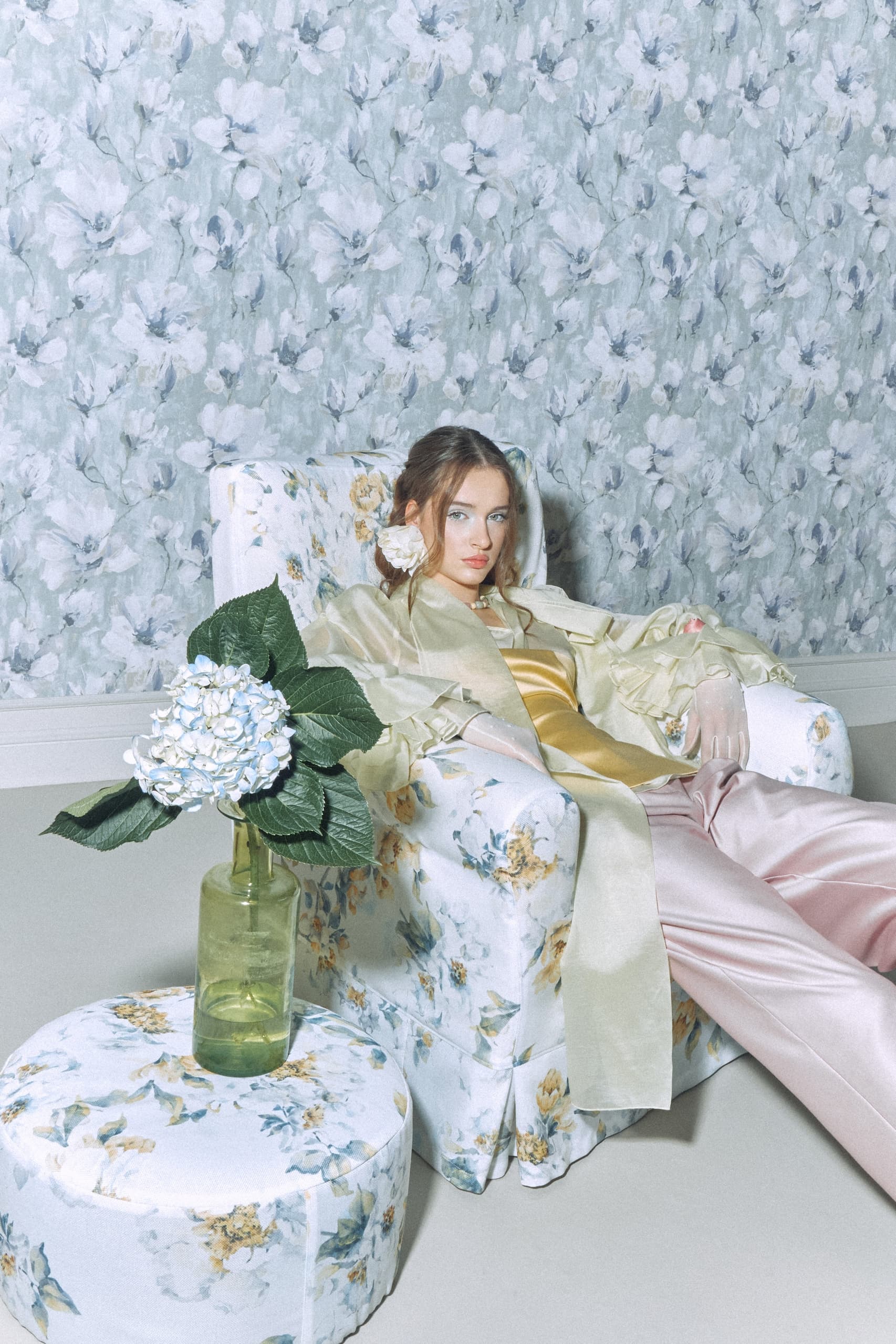 Woman in floral chair with matching decor and hydrangea vase.