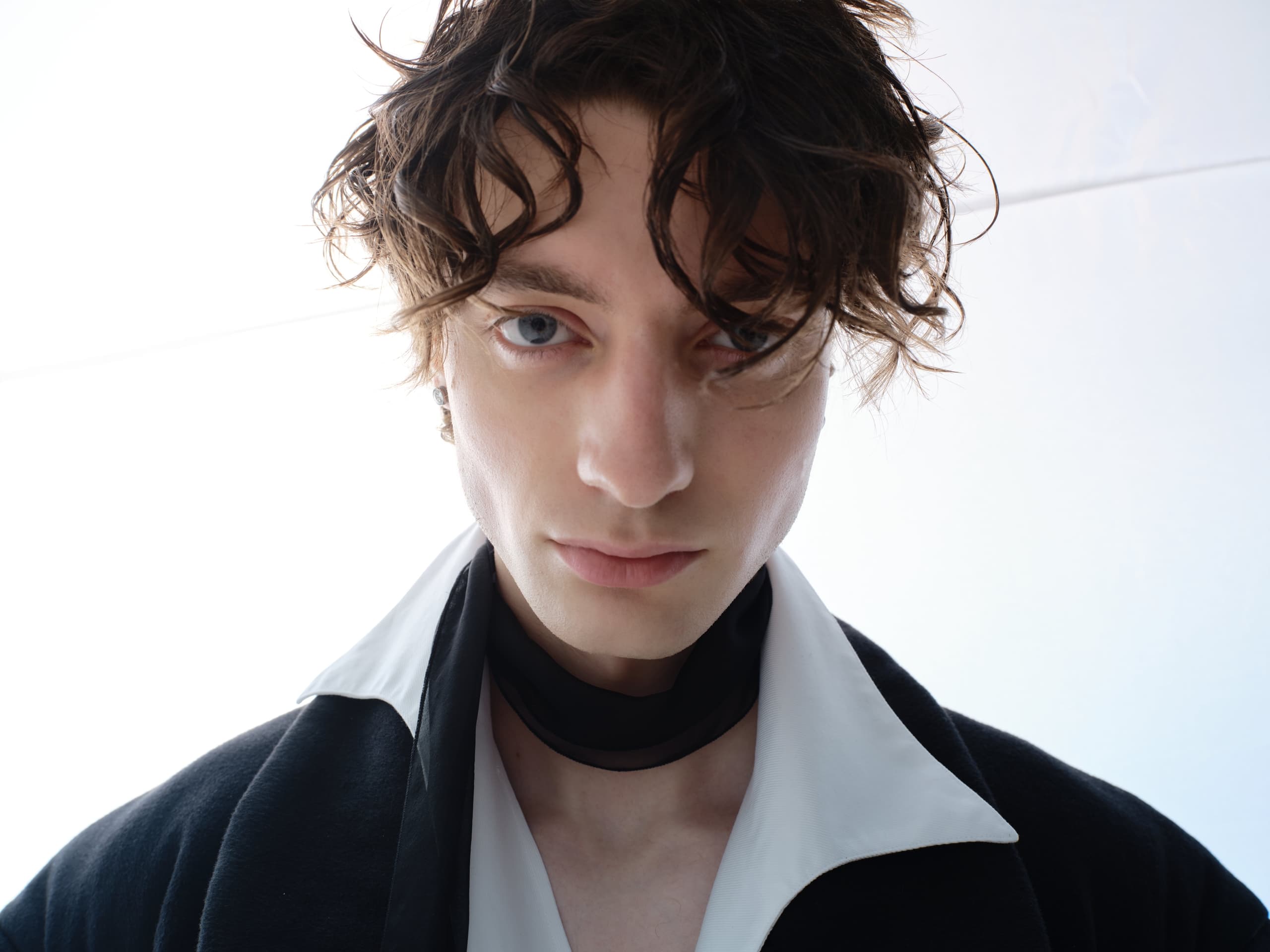 Young model in white shirt with a black collar, gazing intensely at the camera.