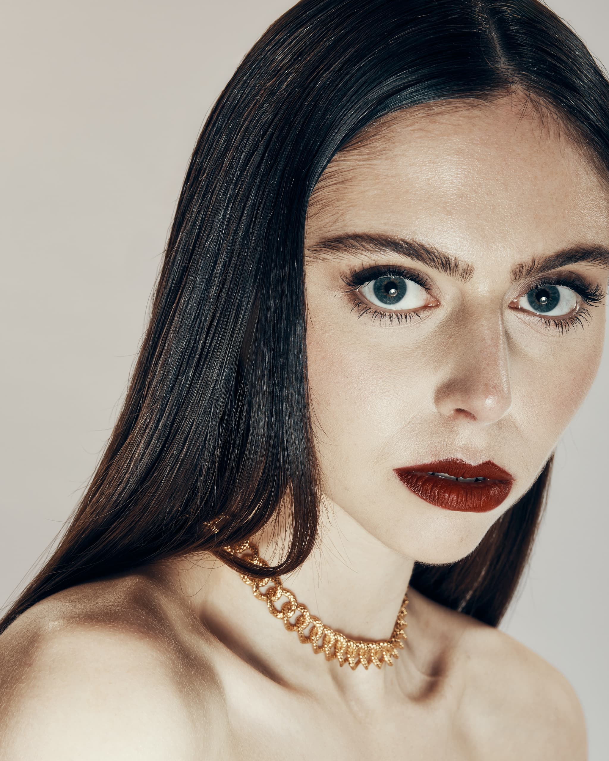 Woman with striking makeup and elegant gold necklace.