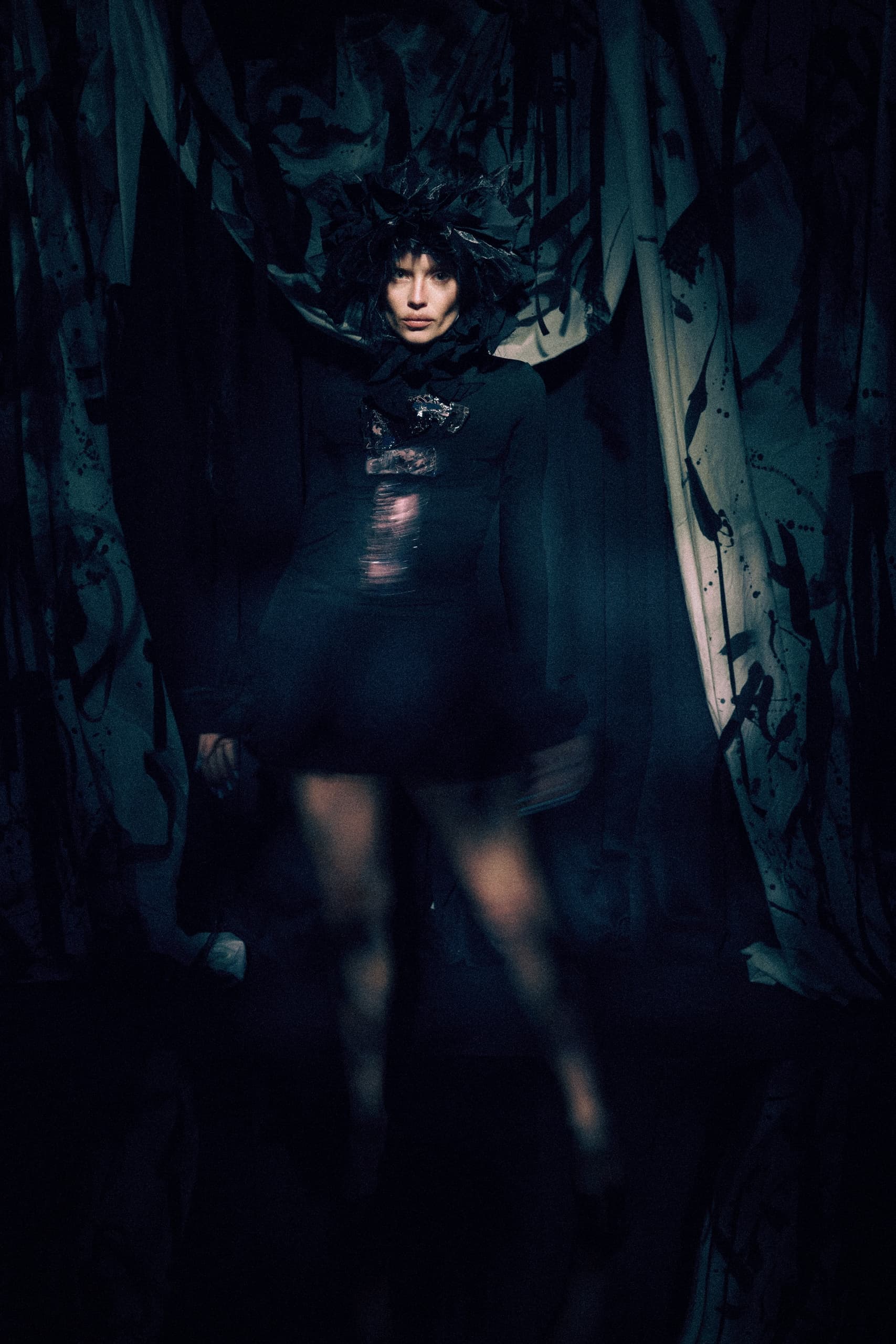 Mysterious figure in dark attire with abstract background and dramatic lighting.
