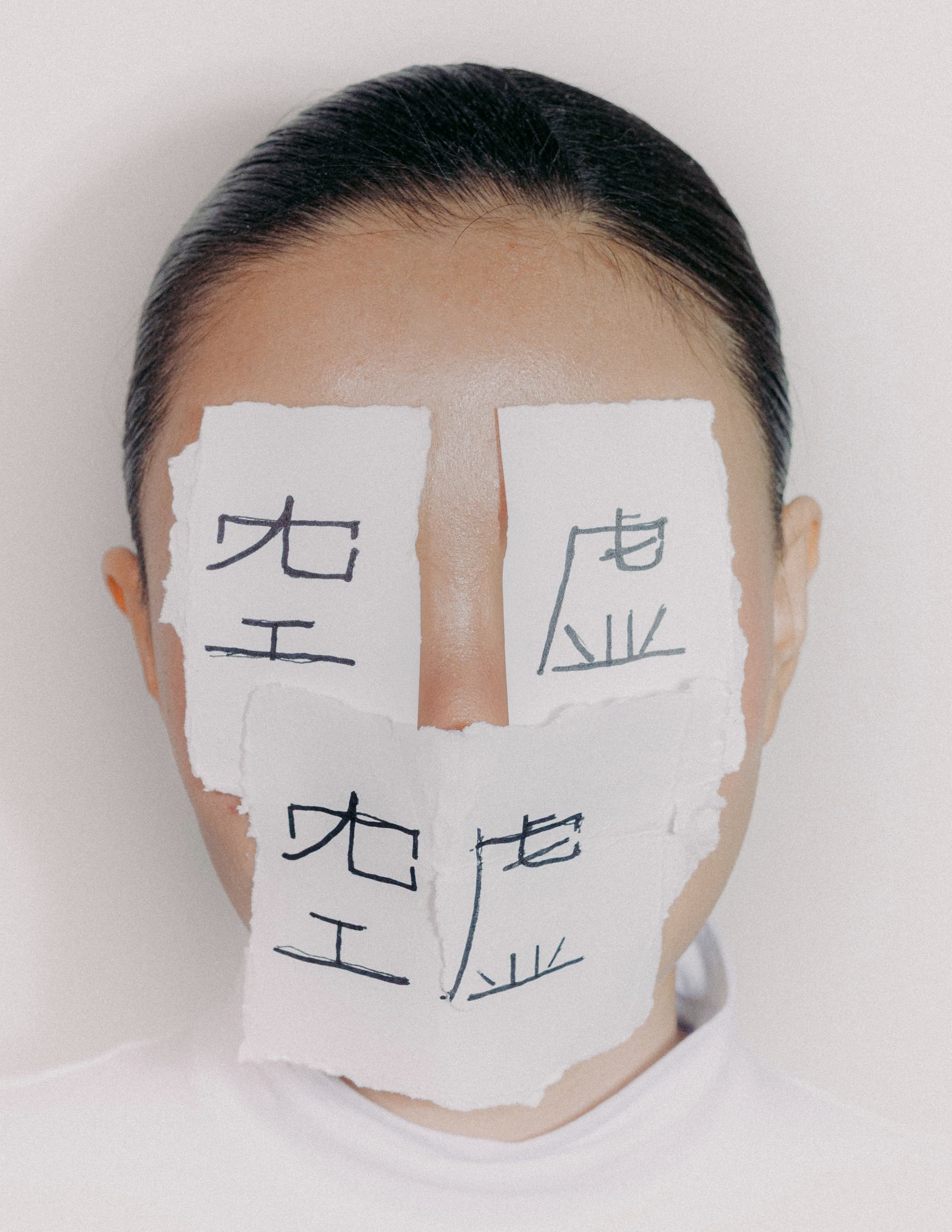 Face covered with handwritten Asian characters on torn white paper pieces.