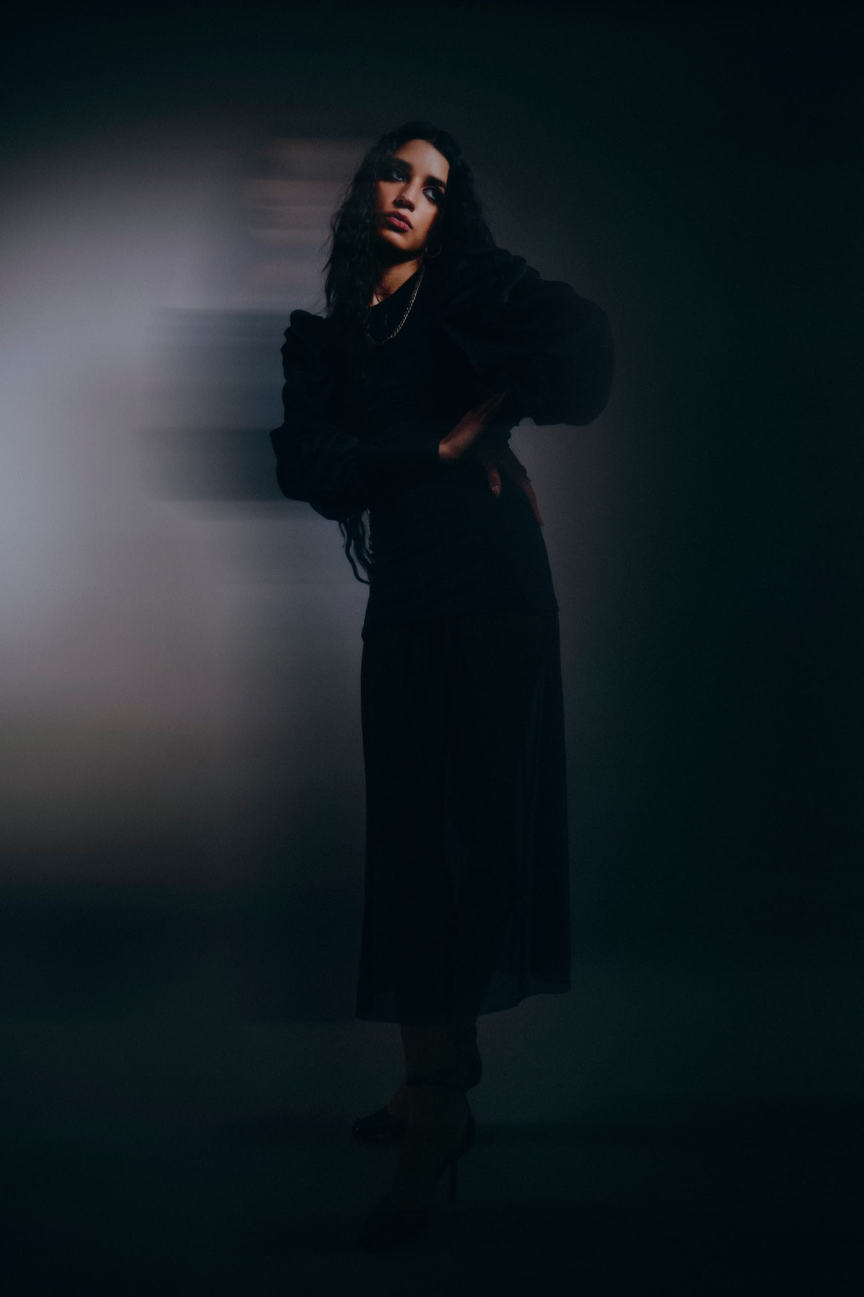 Woman in black dress posing with shadowy effect and dramatic lighting.