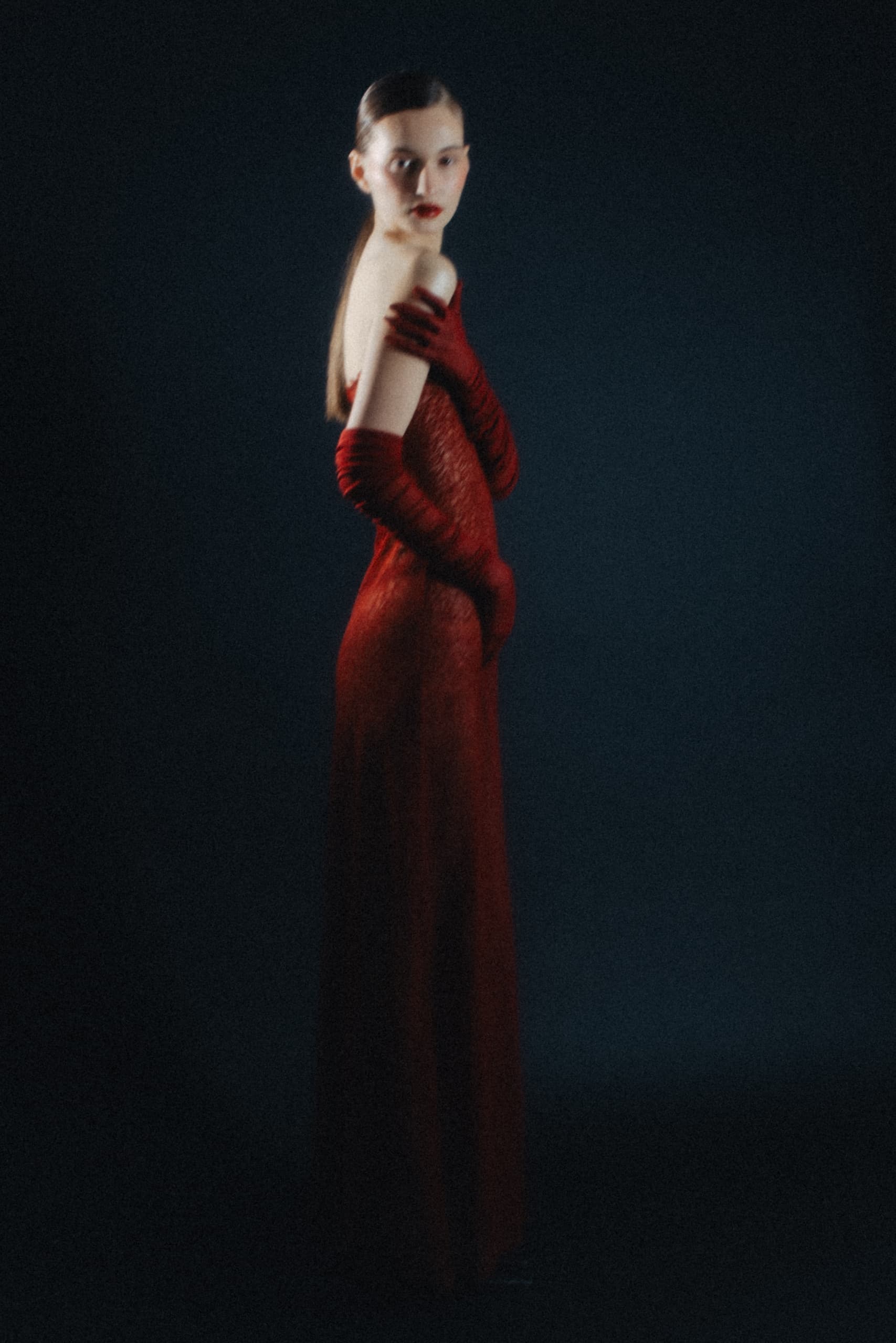 Woman in a red gown and gloves, posing elegantly against a dark background.