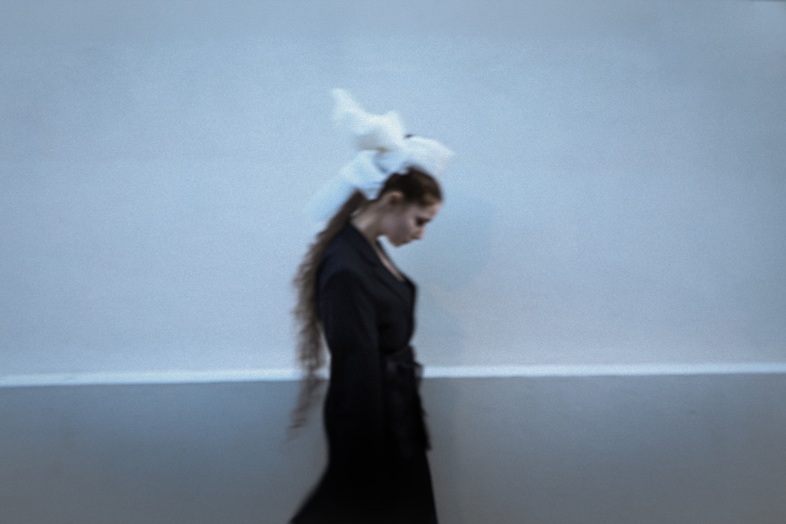 Elegant woman in black with long hair and white headpiece against a blurred background.