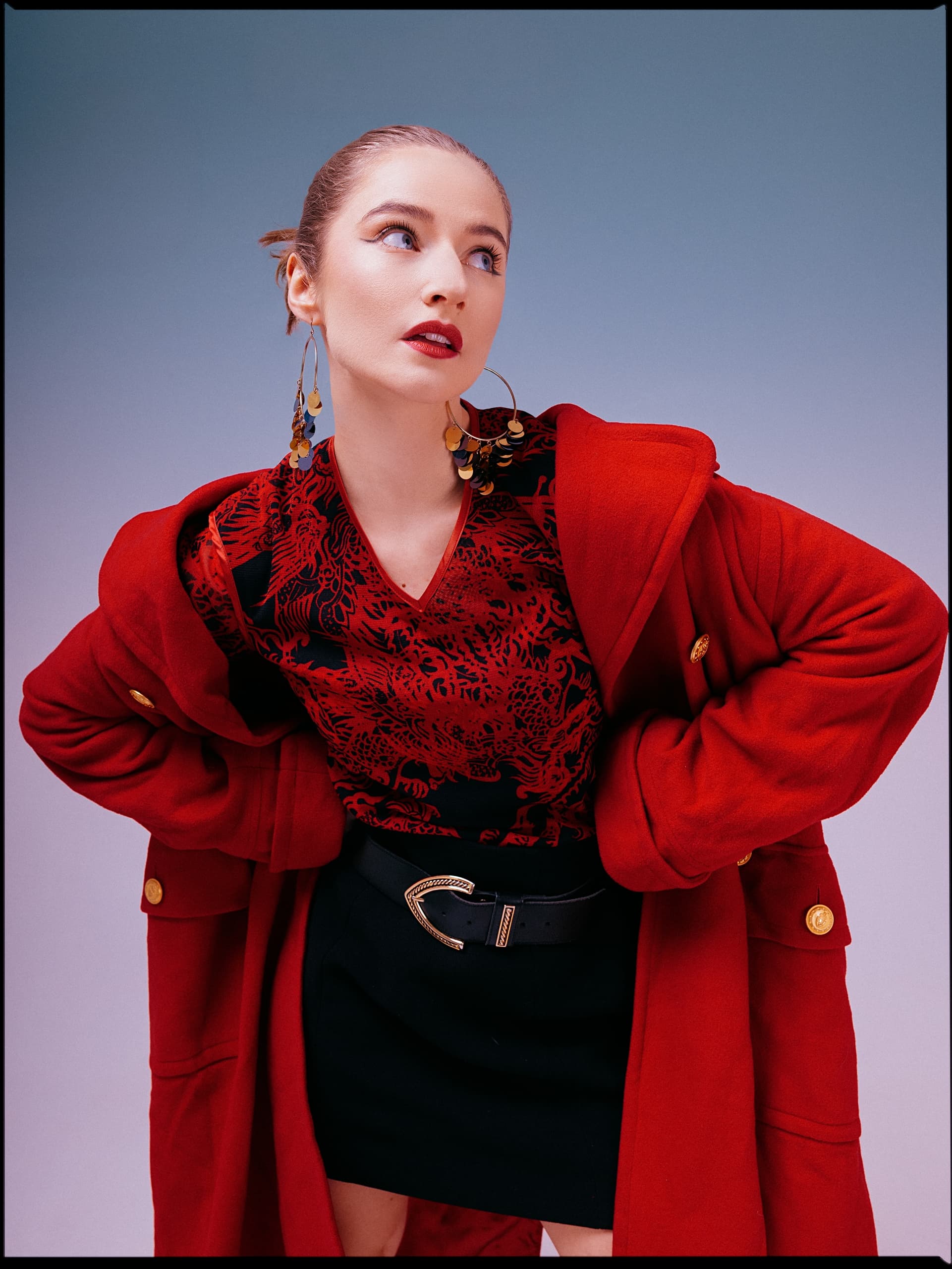 Fashionable woman in red coat and chic earrings, striking a stylish pose.