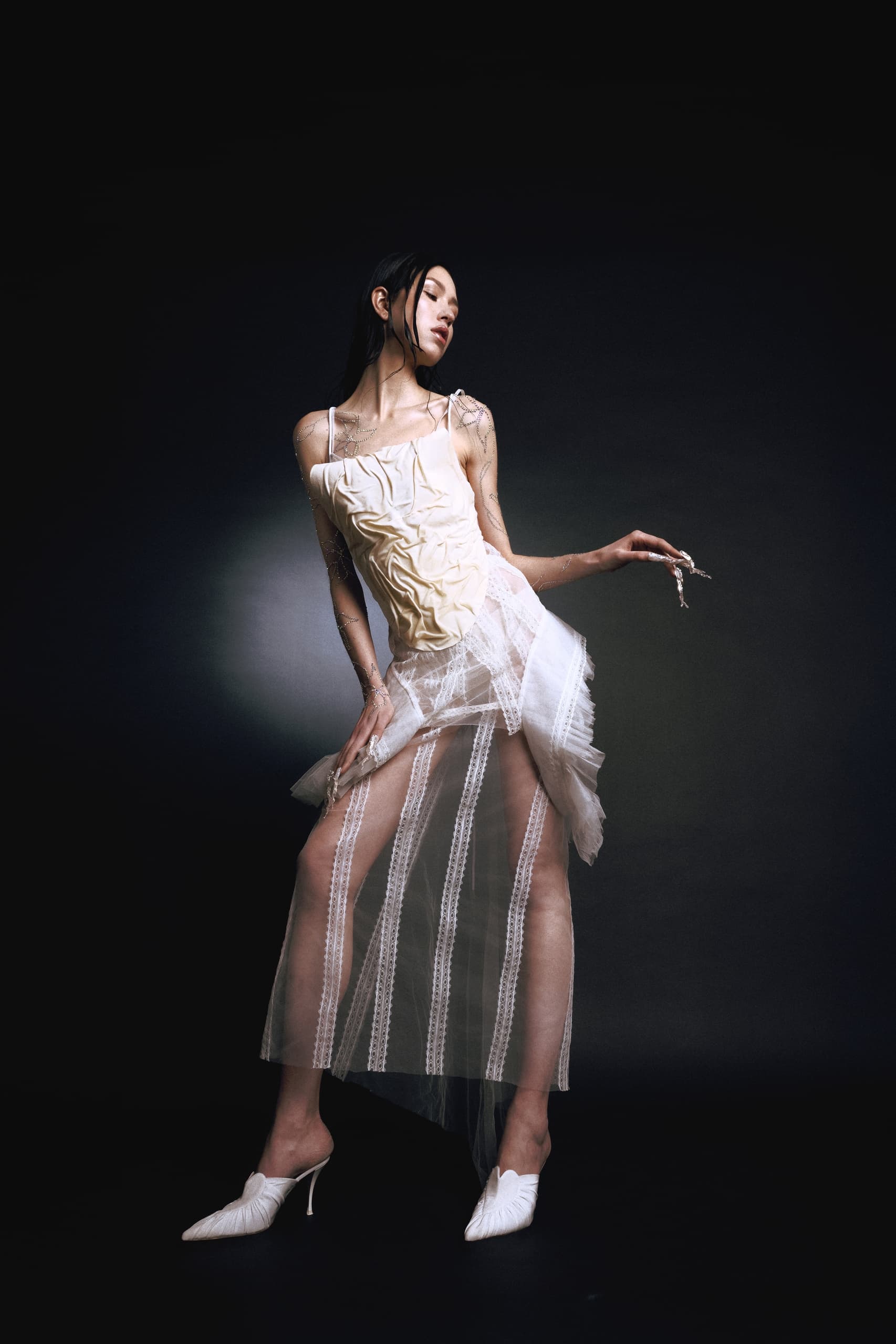 Elegant fashion model in a sheer, artistic dress against a dark background.