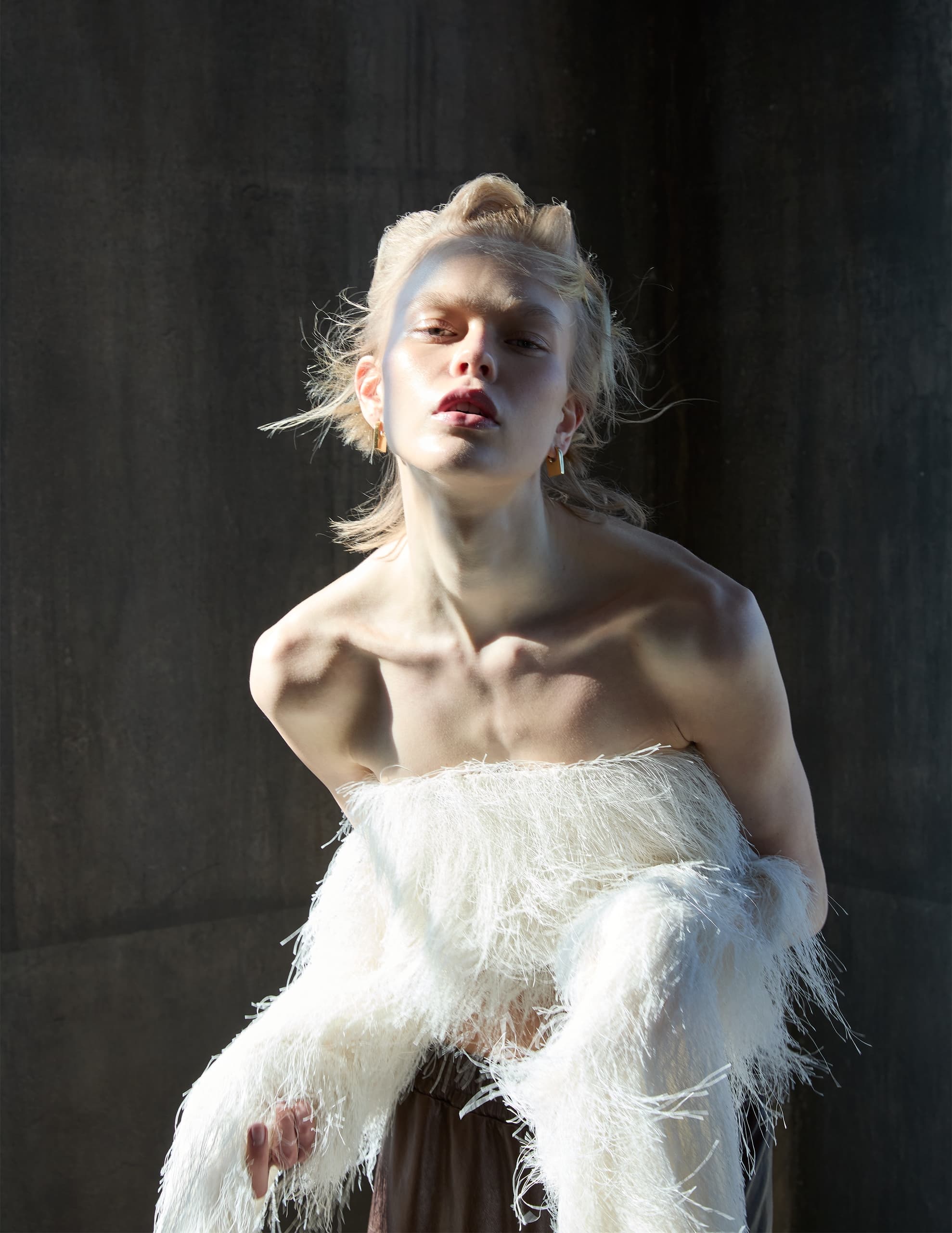 Fashion model in a modern feathered top posing dramatically in soft lighting.
