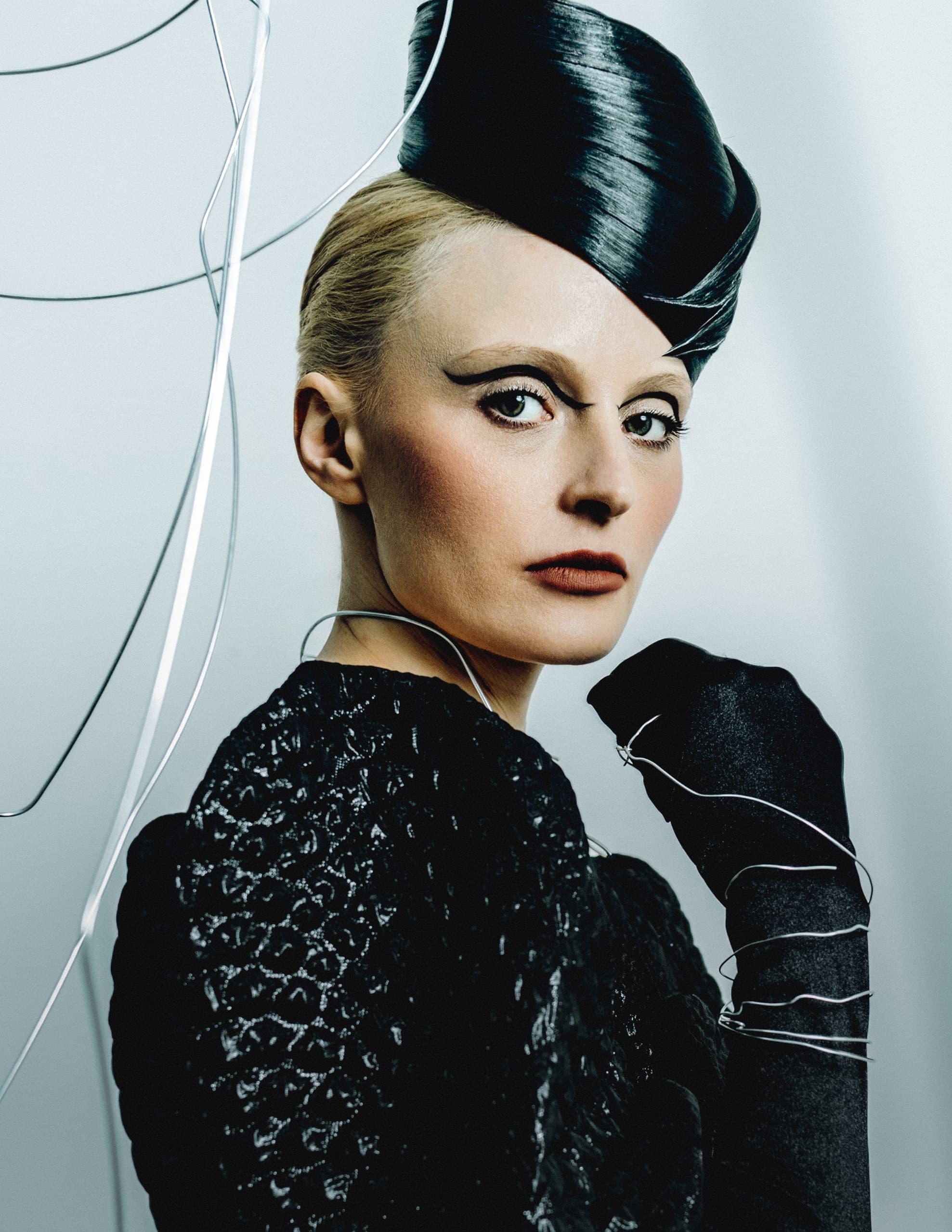 Elegant woman in chic black hat and gloves with artistic wire accents.