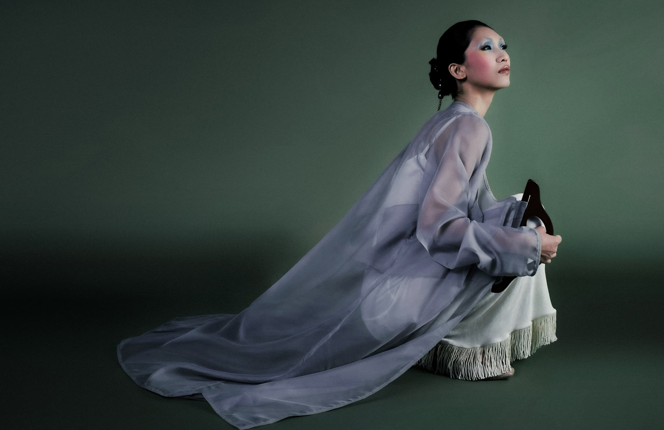 Woman in sheer cape poses gracefully against green backdrop.