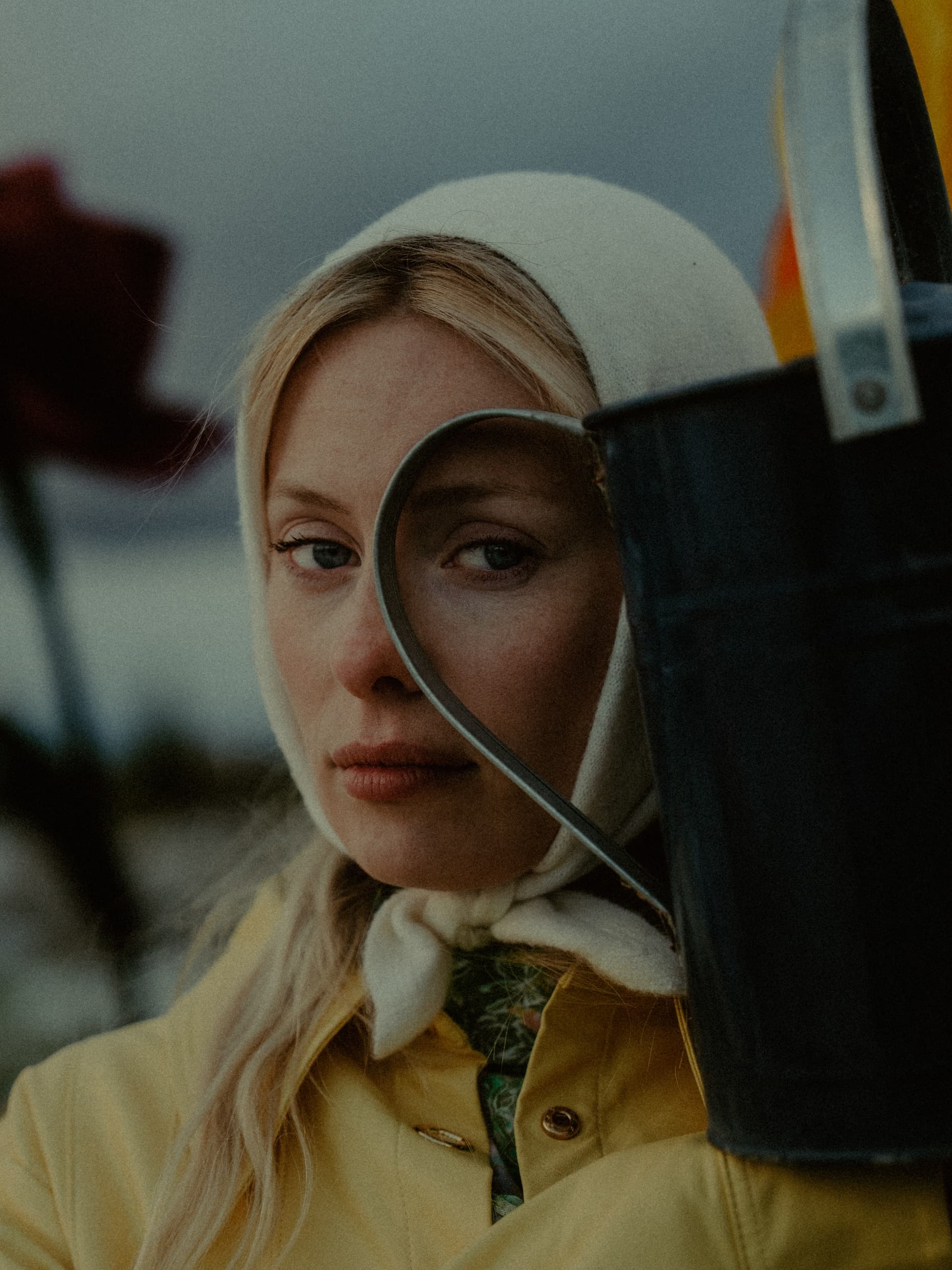 Woman in headscarf with watering can, close-up in a gloomy garden scene.