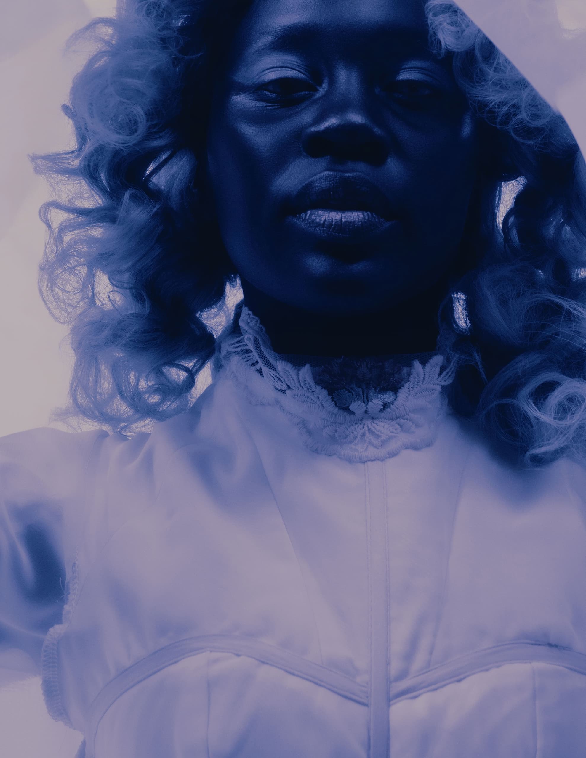 Woman in elegant attire under soft blue lighting, looking serene and composed.