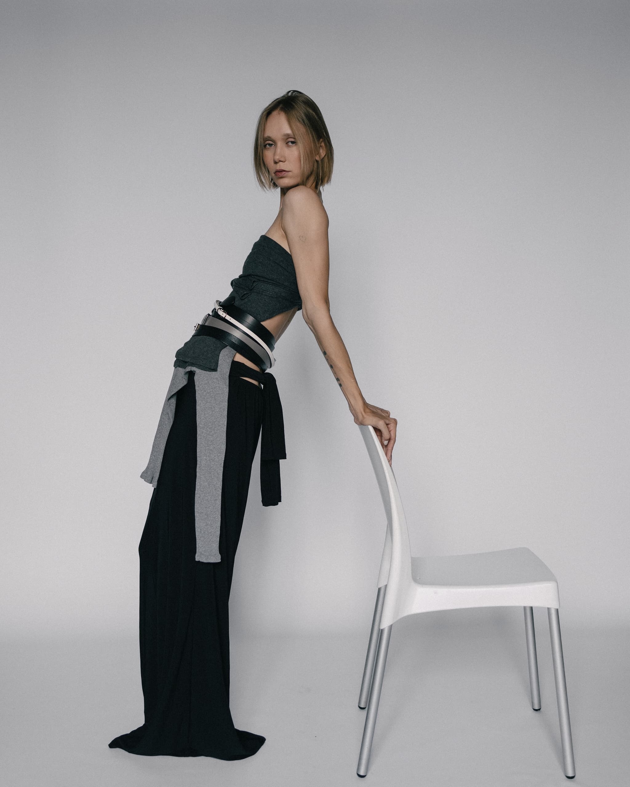 Fashion model posing with a modern chair in a minimalist studio setting.