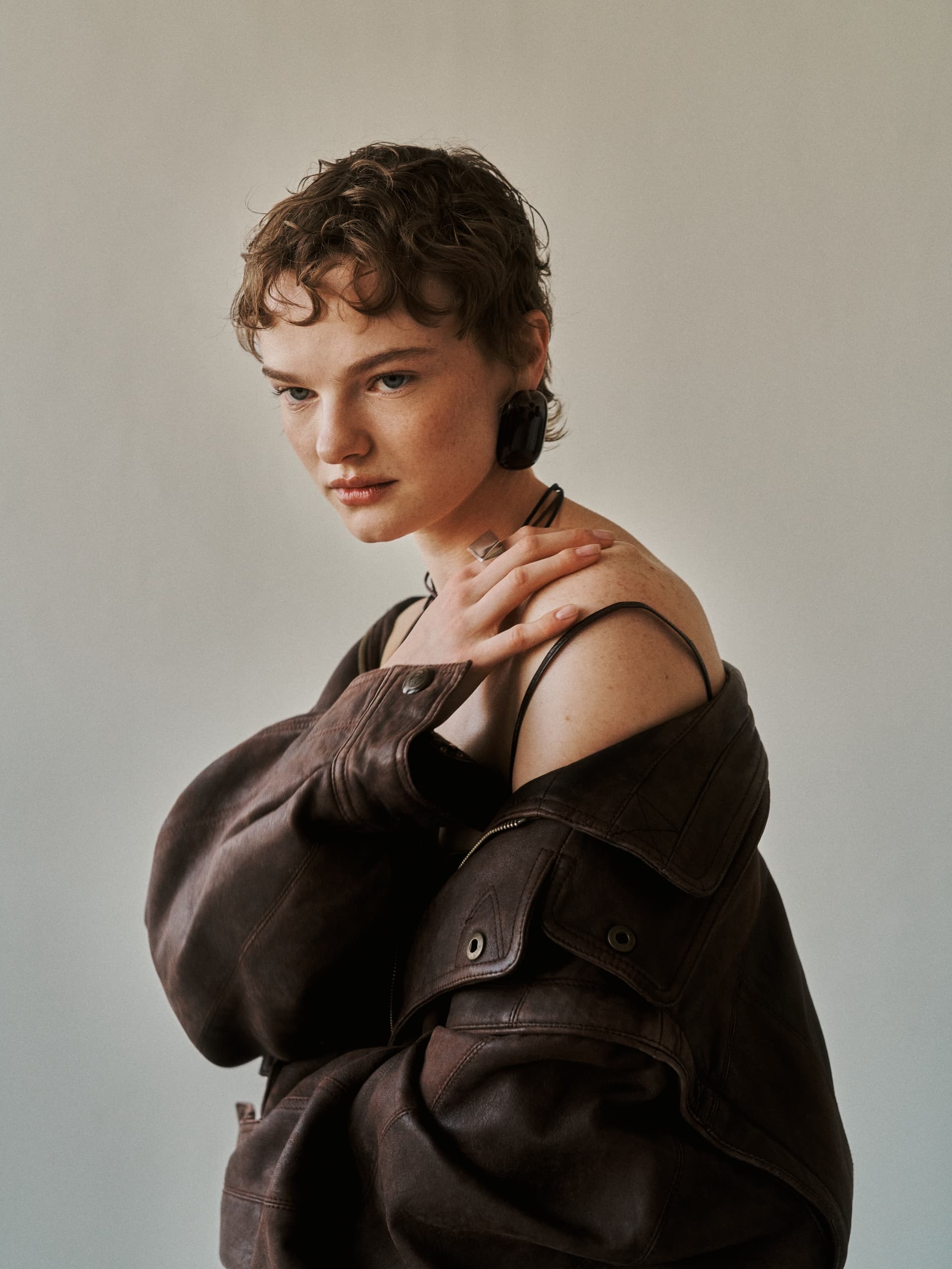 Fashionable person in a brown leather jacket with short hair, striking a pose.