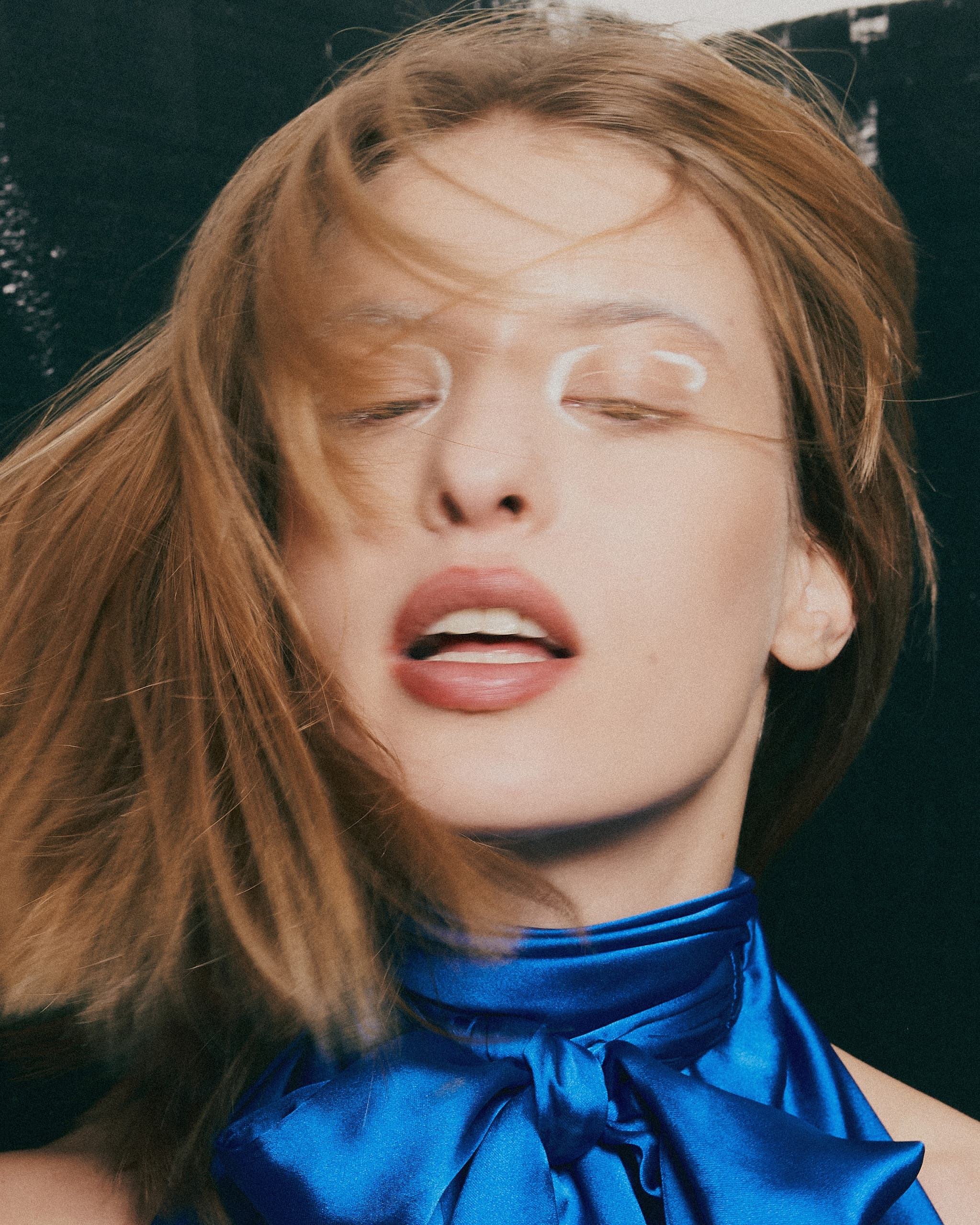 Woman with flowing hair wearing a blue scarf in a fashion photoshoot.
