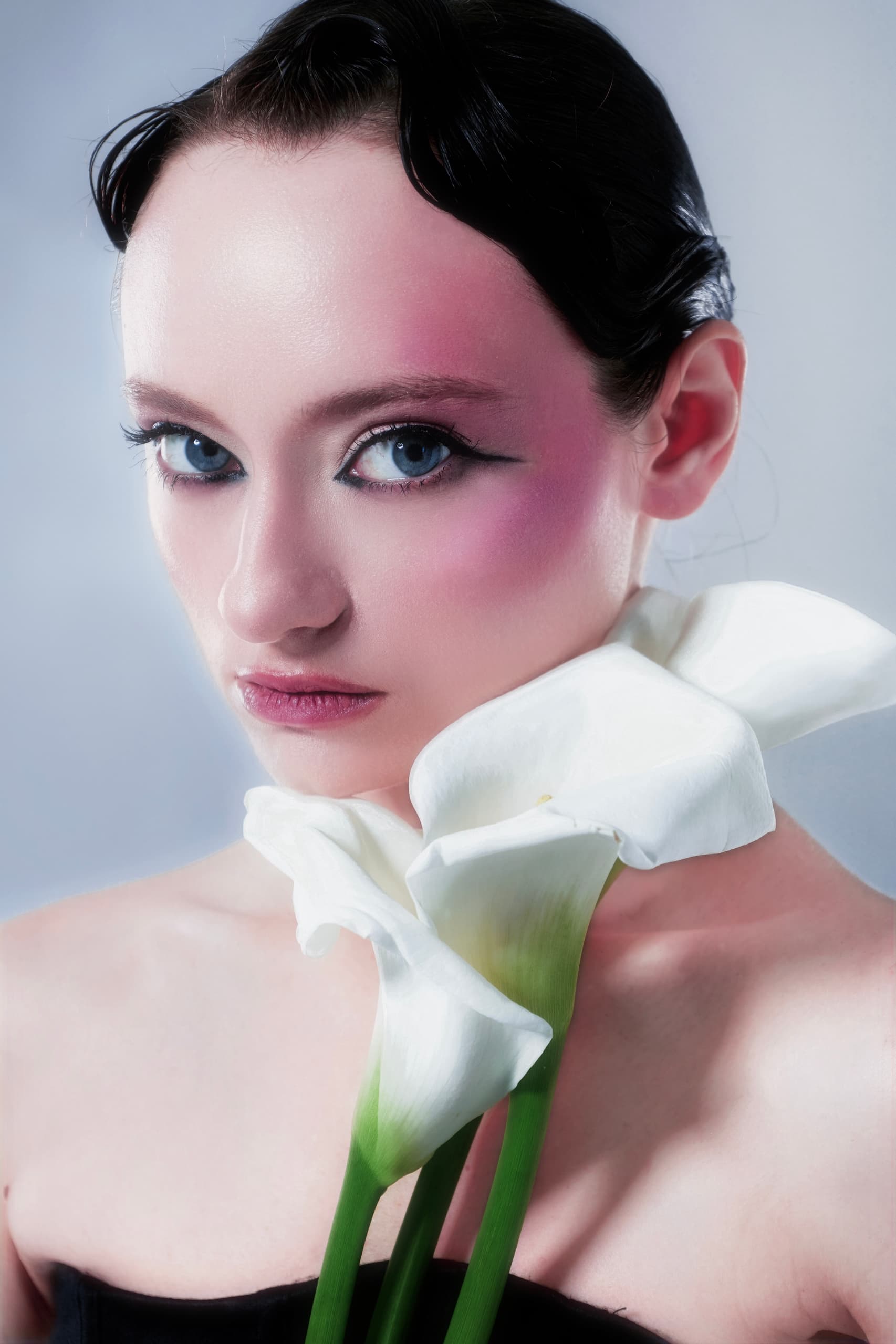 Elegant woman with calla lilies and striking makeup in a studio portrait.